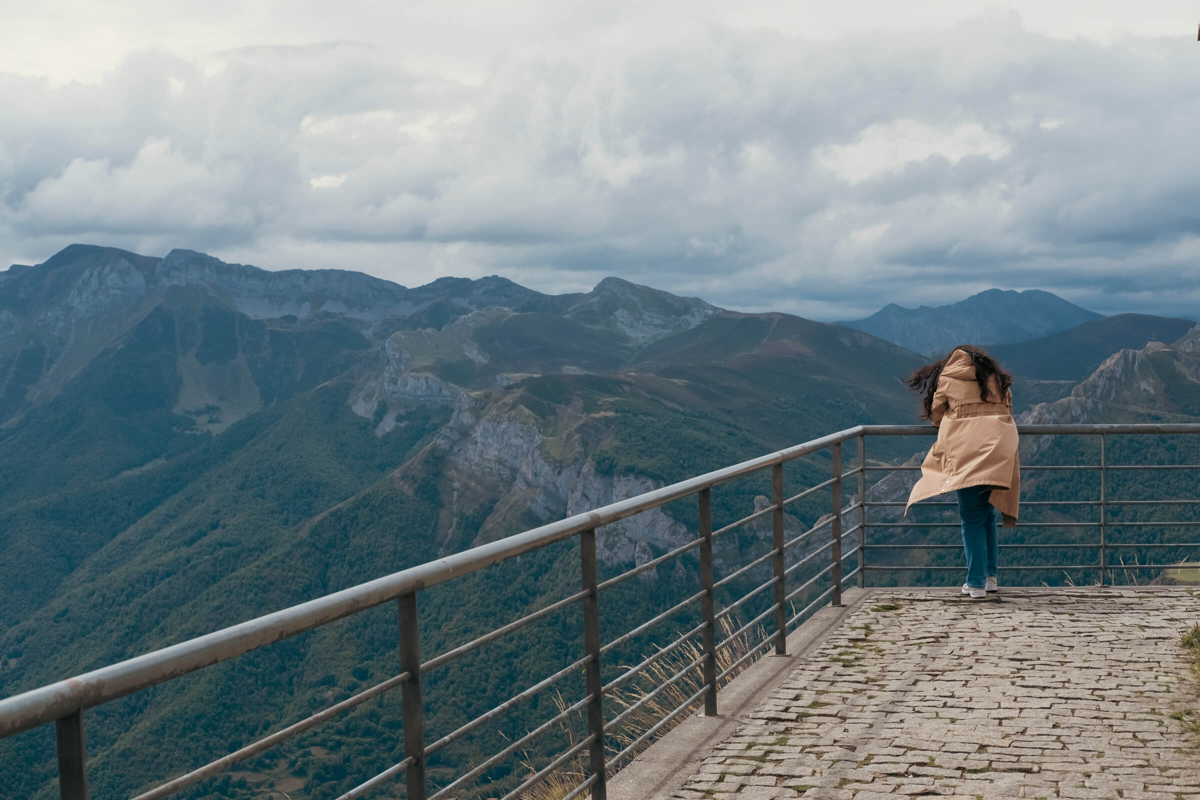 Laura flipando con el paisaje en la parte de arriba del teleférico de Fuente Dé. Mirador hacia el valle de Liébana, con el valle de fondo y una chica de espaldas mirando el paisaje con la gabardina ondeando por el viento
