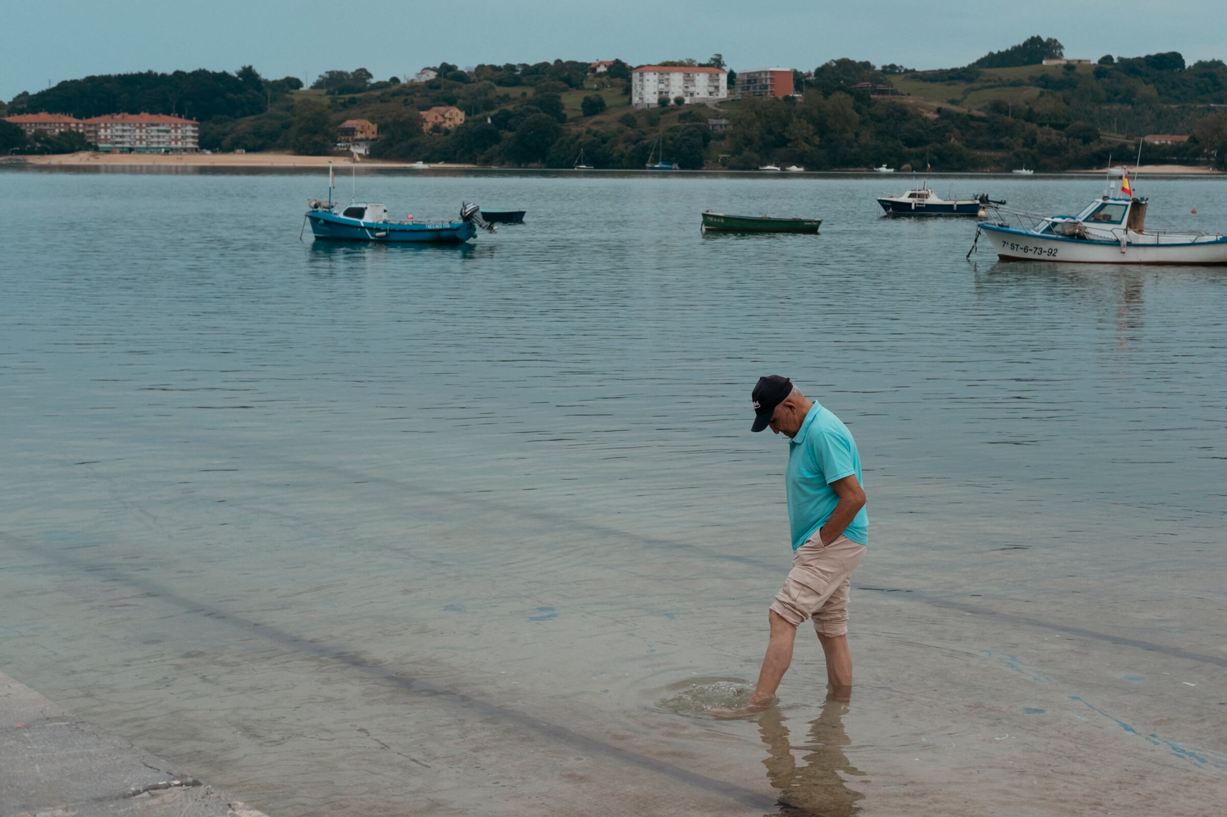 Pensador. Un señor descalzo y de pie en el embarcadero de San Vicente de la Barquera, con los pies metidos en el agua