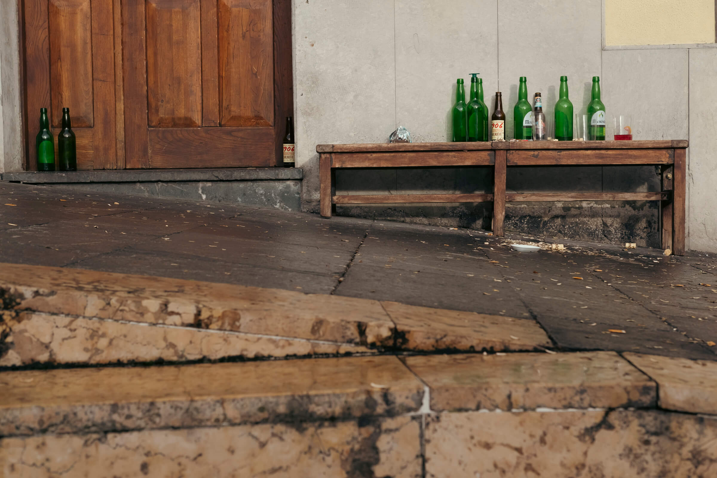 El después. Se ve el 'después' de la fiesta, suelo sucio y banco con botellas vacías