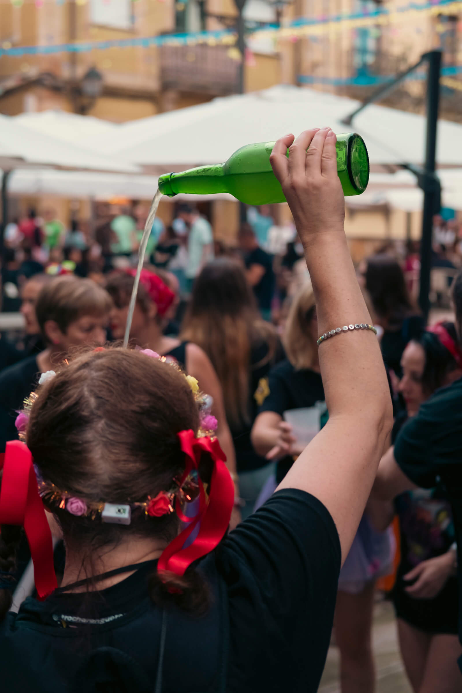 Escanciar: deporte autonómico. En una plaza llena de gente, una chica en primer plano y de espaldas escanciando sidra
