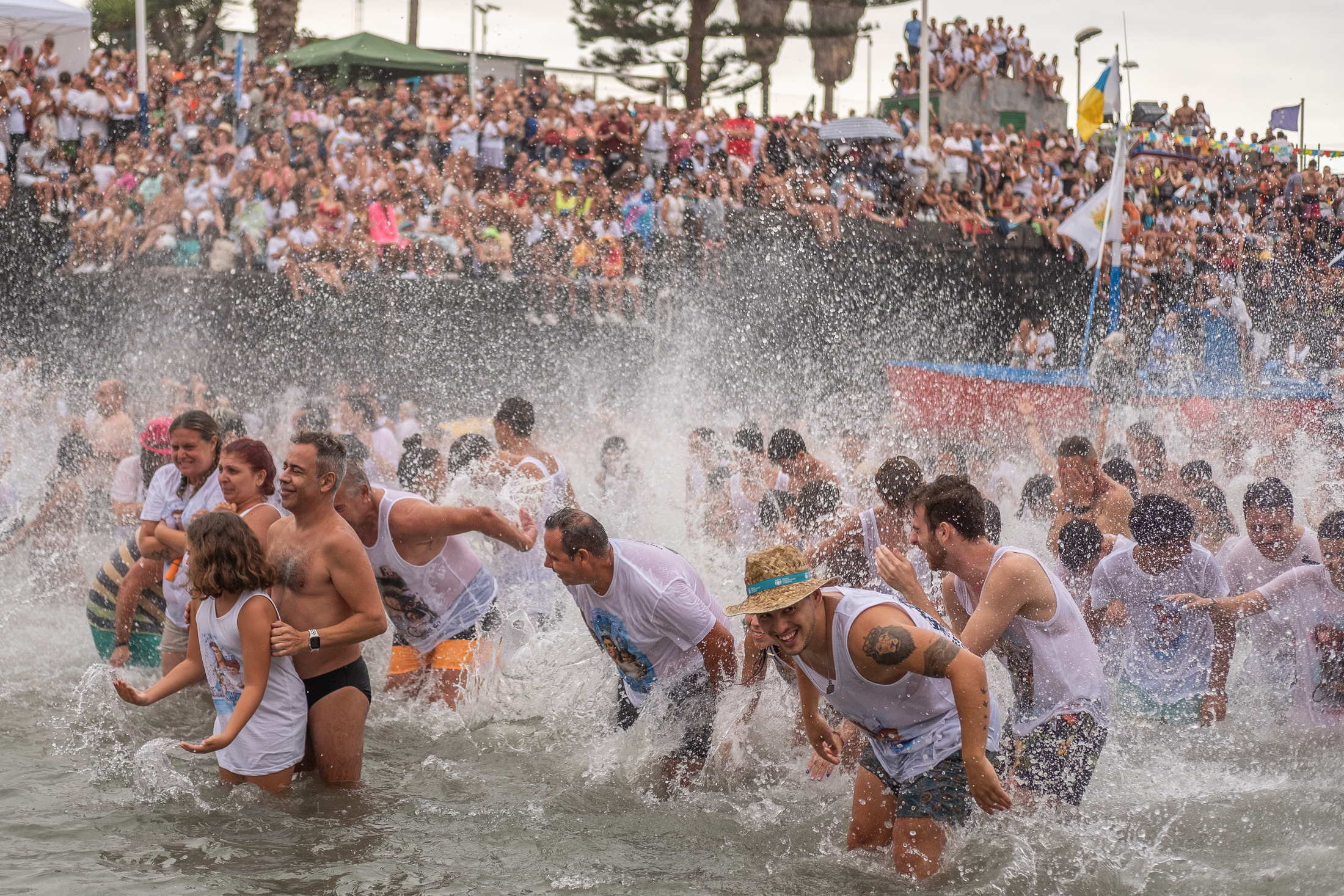 Gente en la playa del muelle, metidos en el mar, salpicando con todas sus fuerzas como bienvenida a la Virgen del Carmen