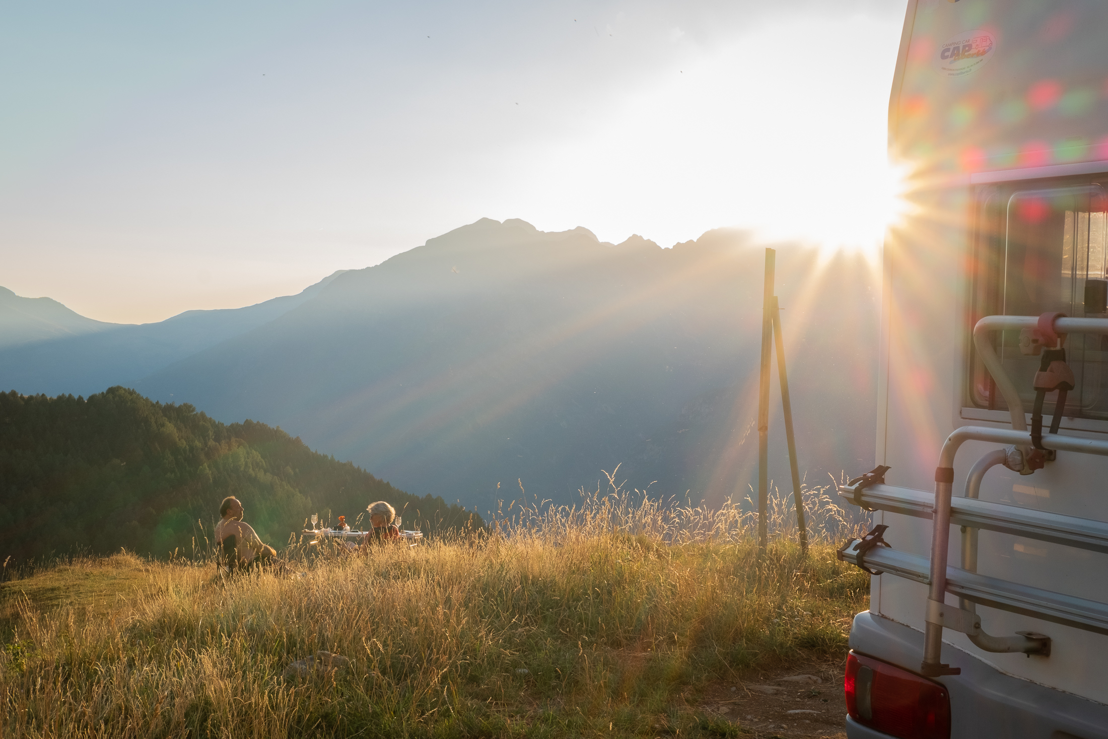 Foto del atardecer desde Cerler, con el valle de Benasque delante y una caravana con una pareja de campistas distrutando de las vistas y la tranquilidad del momento
