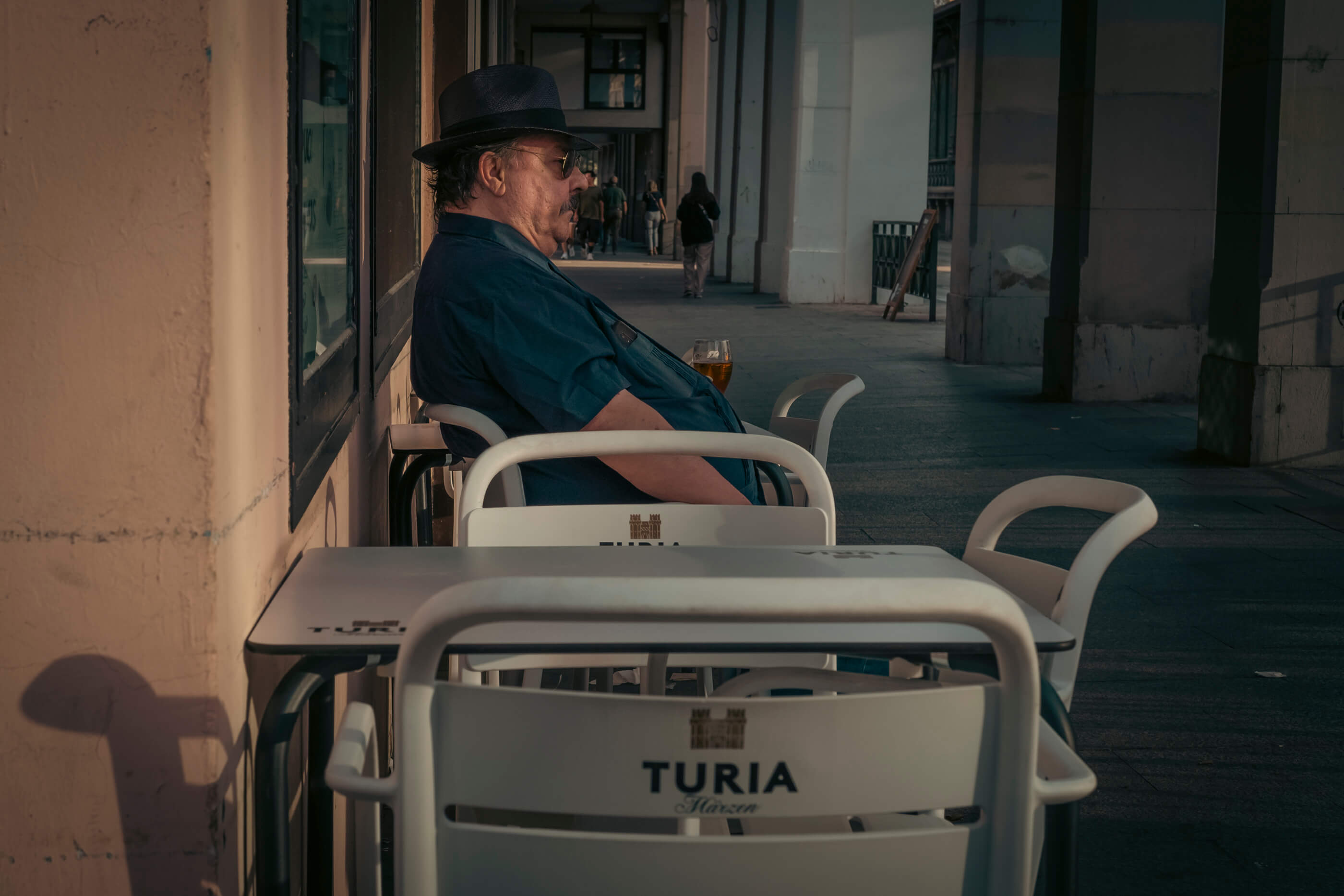 Señor de perfil, con sombrero y gafas de sol, tomándose una copa de cerveza en una terraza