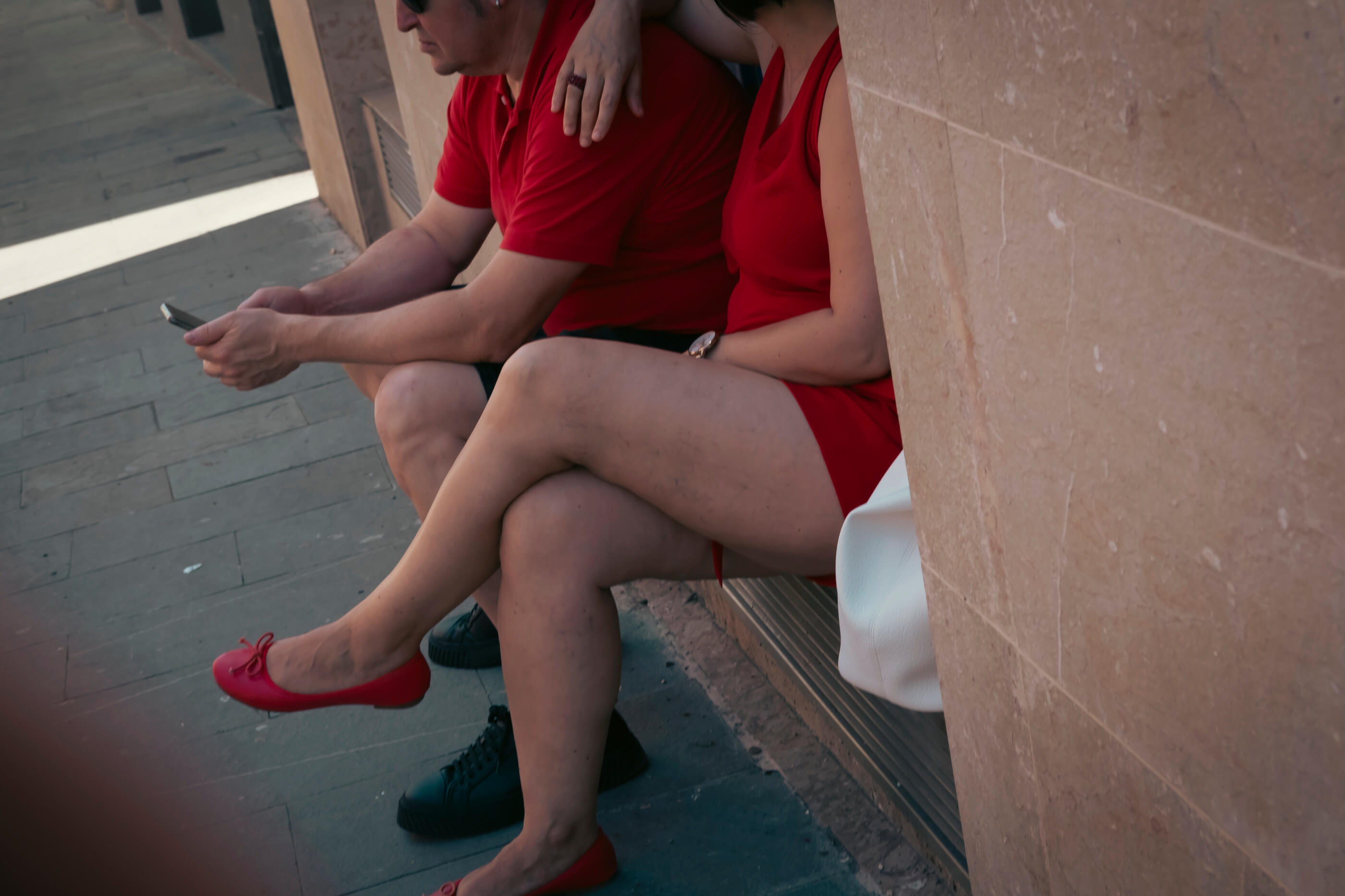 Todo al rojo. Una pareja esperando sentados en un escalón, él con polo rojo y ella con vestido y tacones del mismo rojo