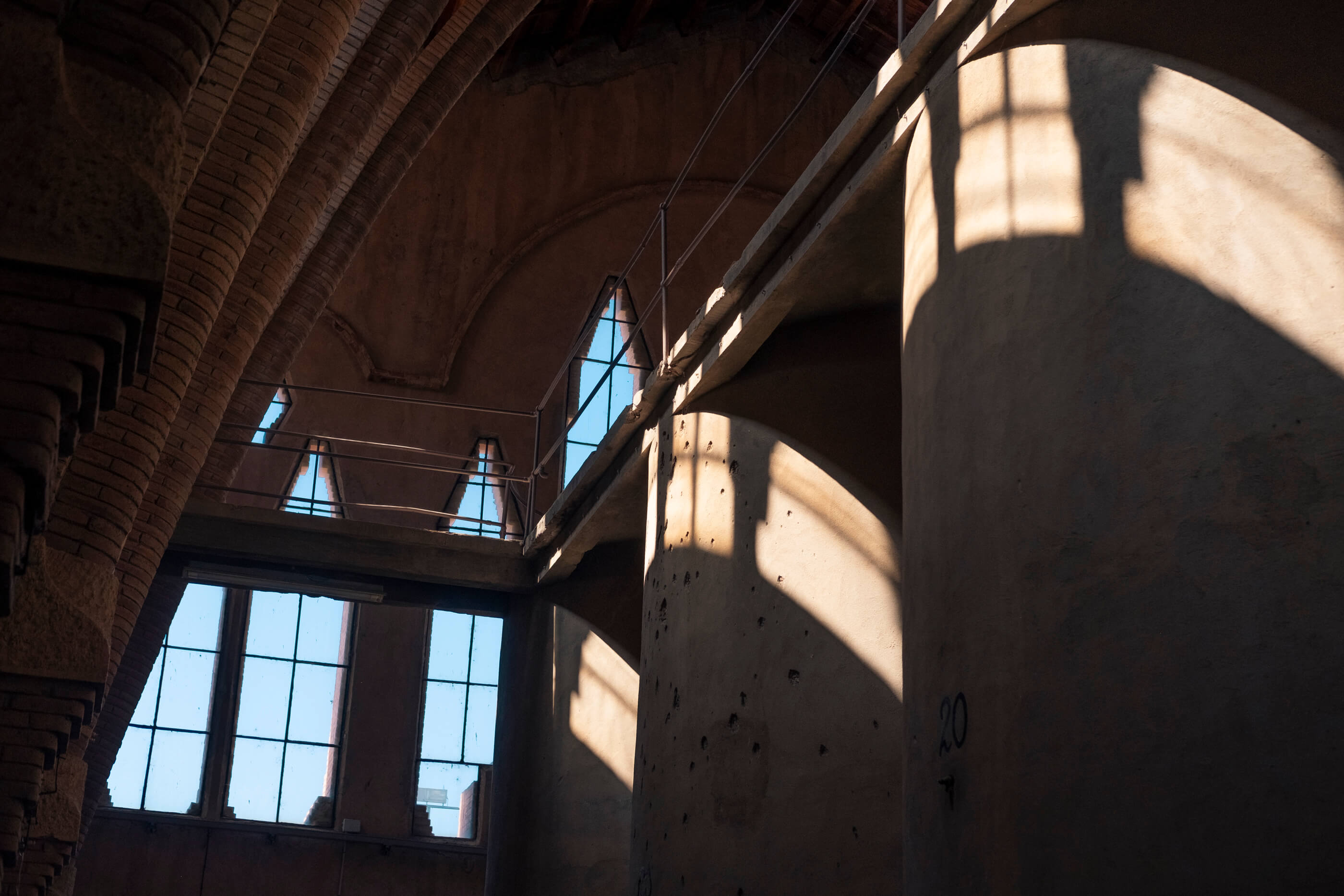 Luz entrando por los ventanales de La Catedral del Vino, bodega en Pinell de Brai. Un edificio antiguo con unos enormes depósitos de vino construídos en hormigón, unos grandes ventanales de fondo y el sol iluminando el interior de la estancia creando zonas de luces y sombras