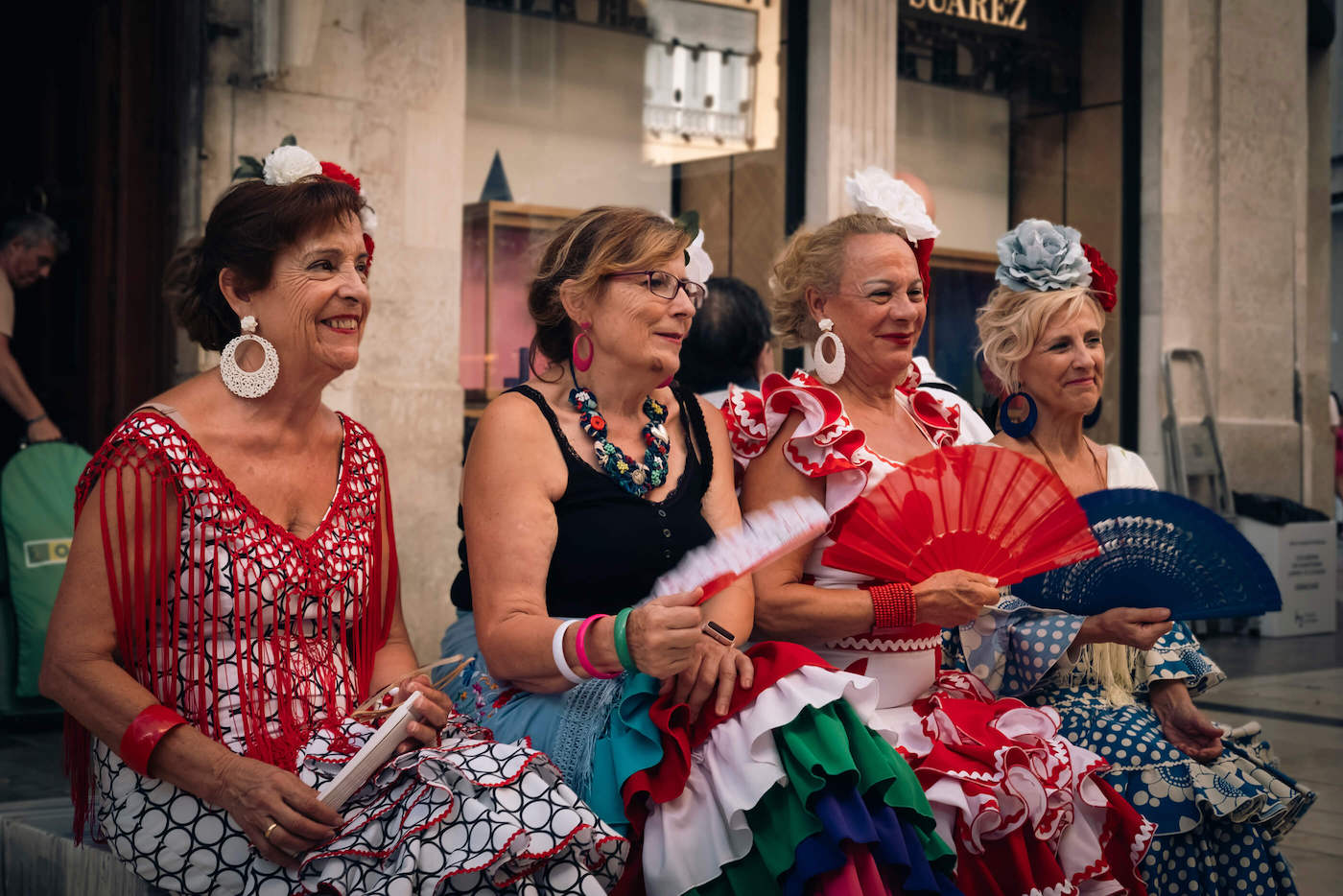 Señoras malagueñas posando en la calle con sus vestidos coloridos de fiesta, abanicos y sus floripondios en el pelo, típicos de la feria malagueña.