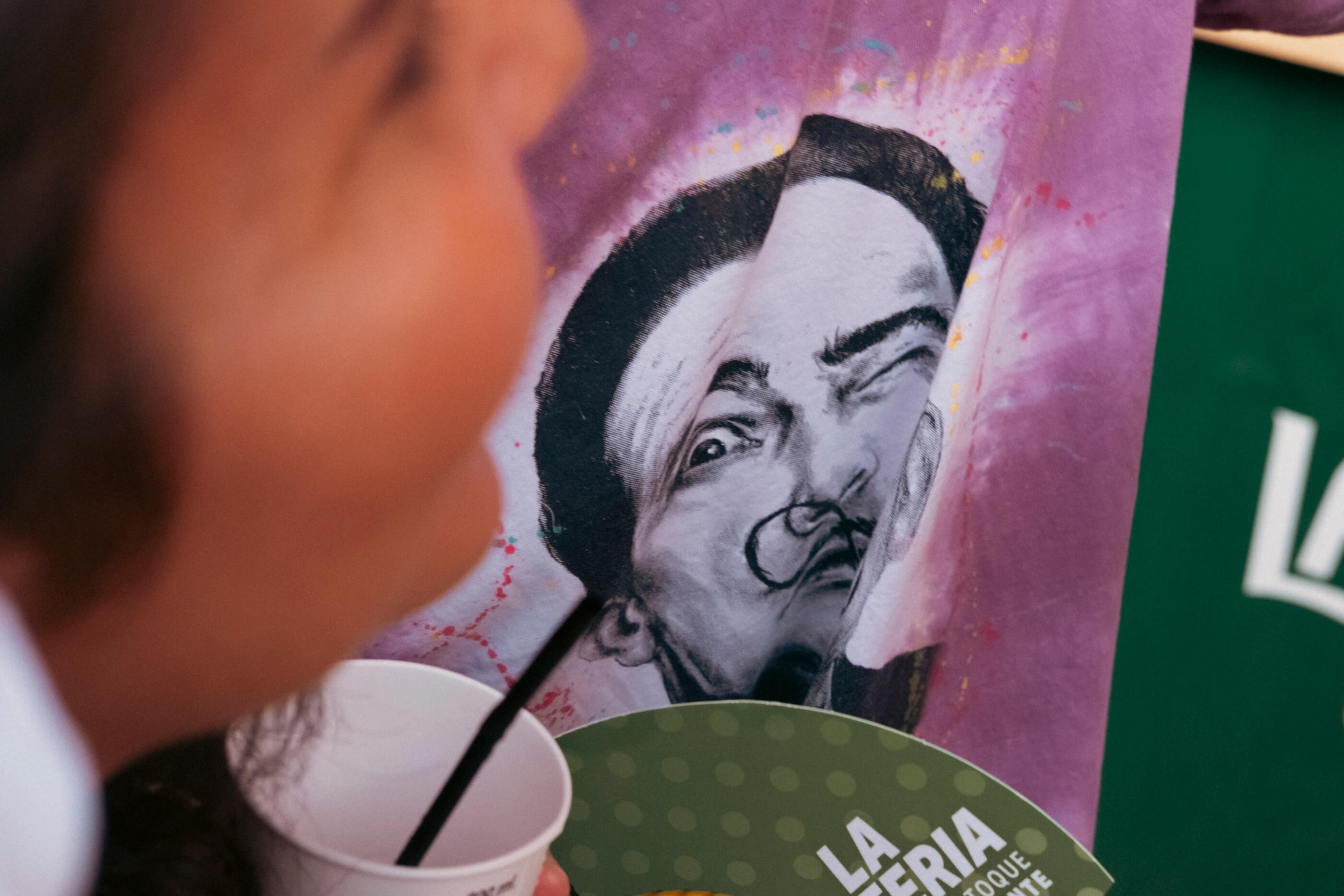 No te pases que te vigilo. Se ve la silueta de una chica desenfocada a un lado y de frente, enfocada, la cara de Dalí y su mirada desafiante ilustrada en una camiseta de otra persona