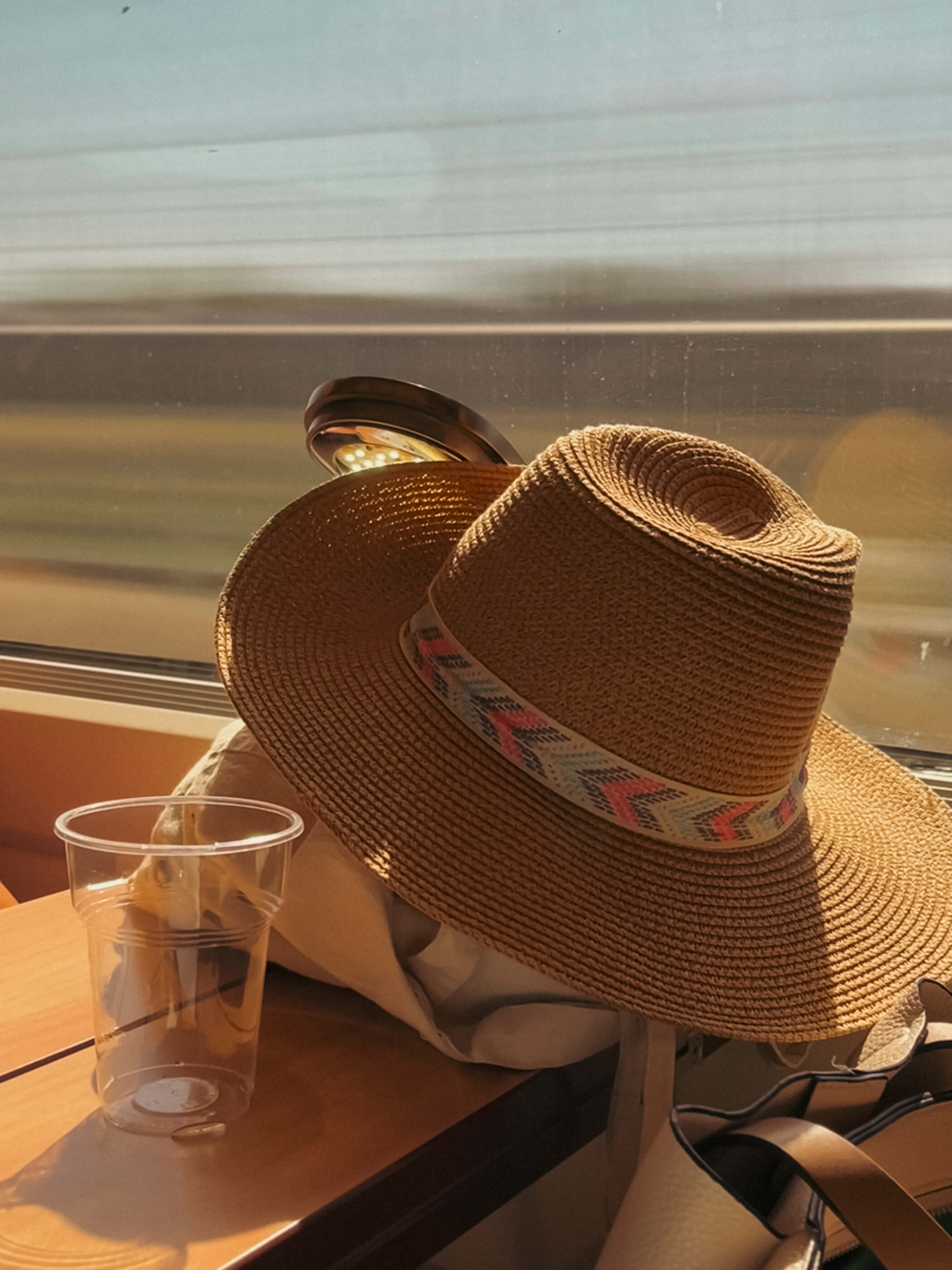 Viajando a alta velocidad. Un sombrero sobre una mochila y un vaso vacío sobre la mesa de un tren de alta velocidad, tomada con larga exposición para que se aprecie por la ventana el paisaje desenfocado por la velocidad