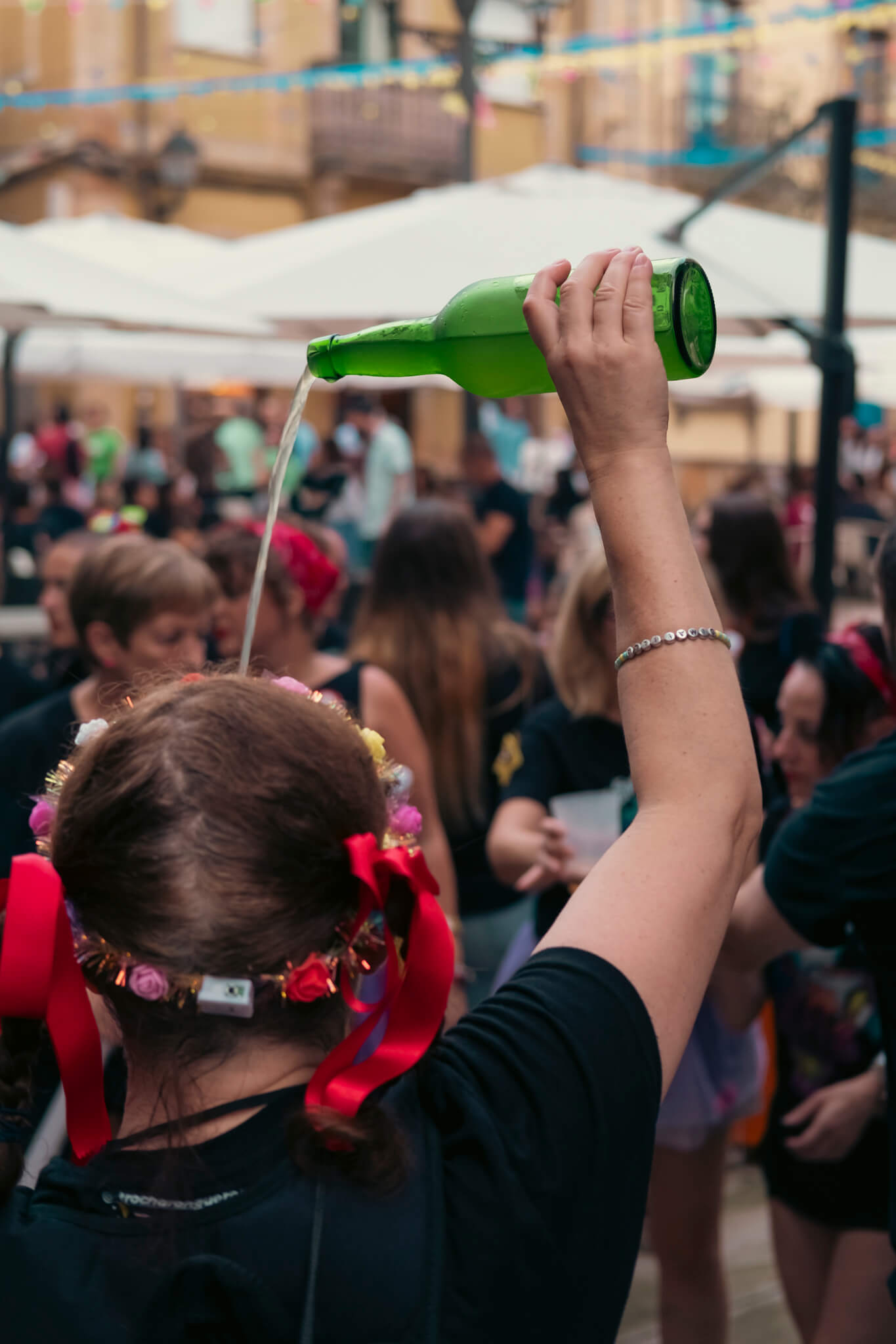 Escanciar: deporte autonómico. En una plaza llena de gente, una chica en primer plano y de espaldas escanciando sidra