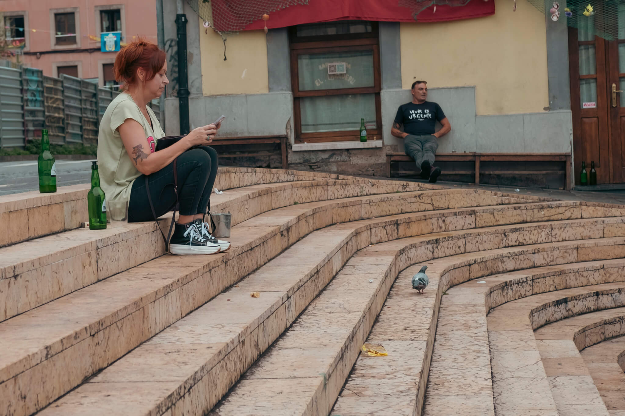 Las escaleras de la plaza del Lavadero. Unas escaleras en las que una chica está sentada revisando su móvil y bebiendo sidra mientras otra persona está al fondo a su aire