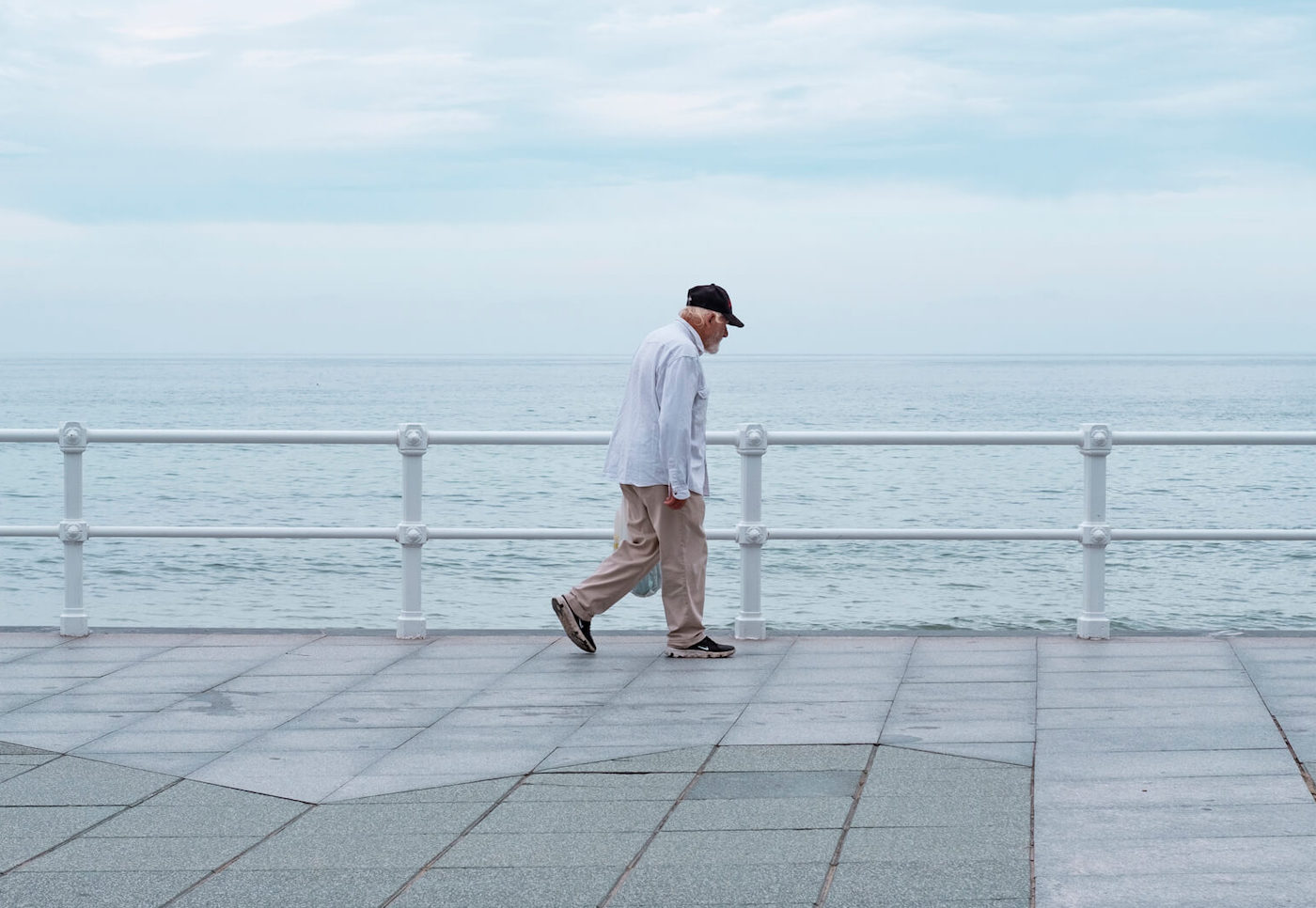 Señor caminando por el paseo de Gijón, se le ve avanzando de izquierda a derecha y encuadrado en el centro, con un color azul grisáceo en el cielo.