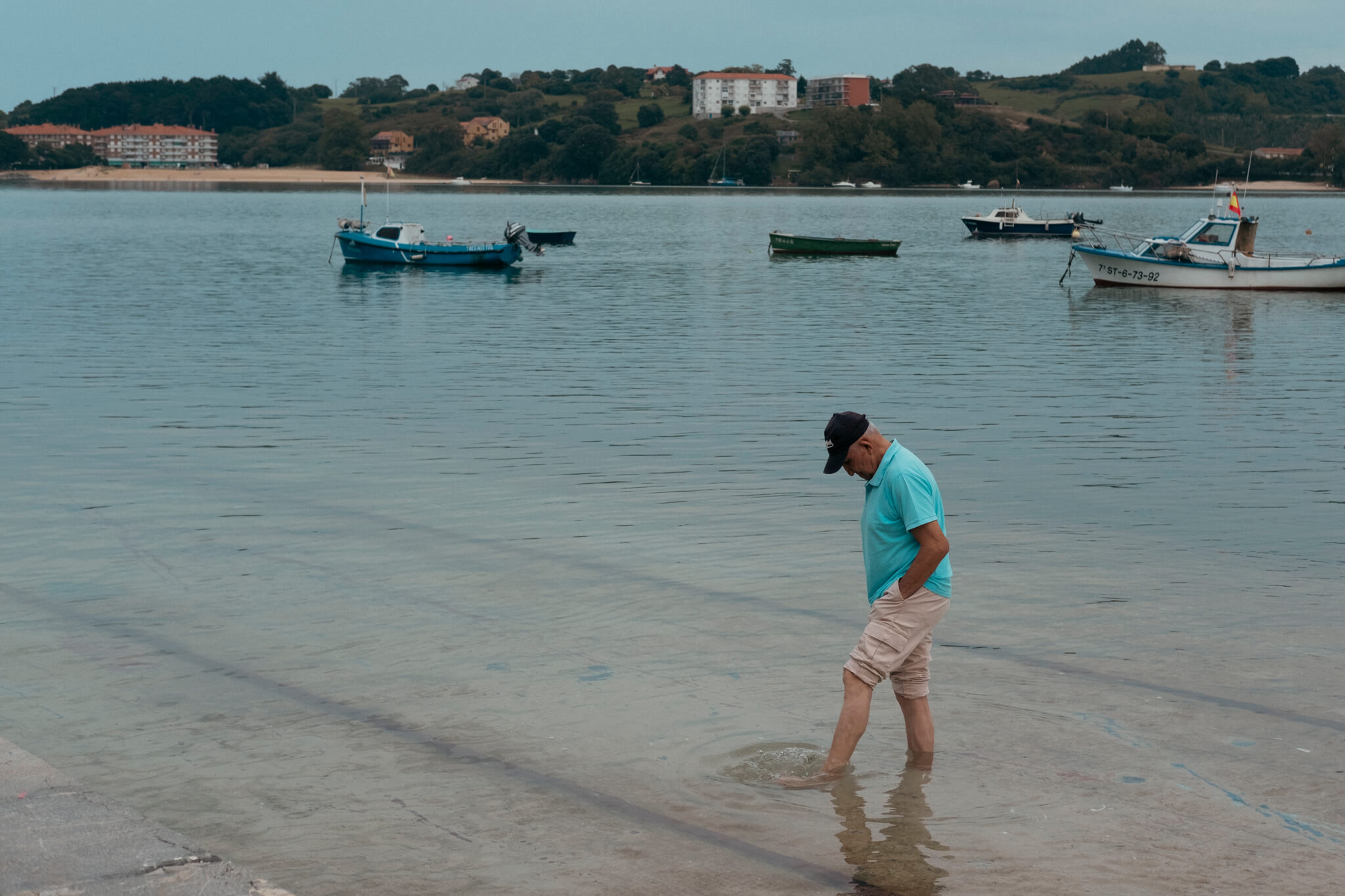 Pensador. Un señor descalzo y de pie en el embarcadero de San Vicente de la Barquera, con los pies metidos en el agua