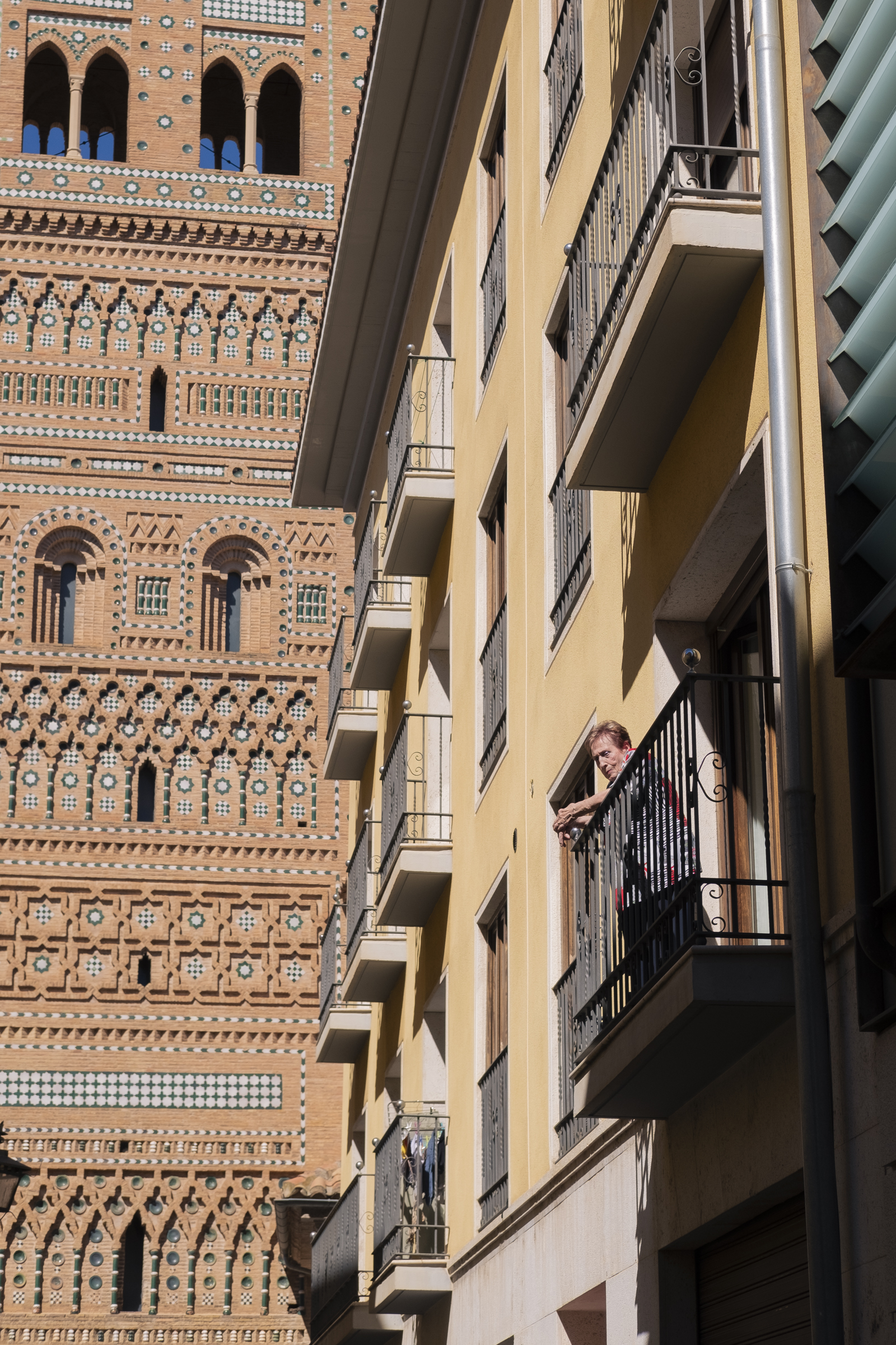 Señora en el balcón y torre Mudéjar de fondo (Teruel). Se ve una señora en un balcón echando un vistazo a la calle y una torre mudéjar de fondo