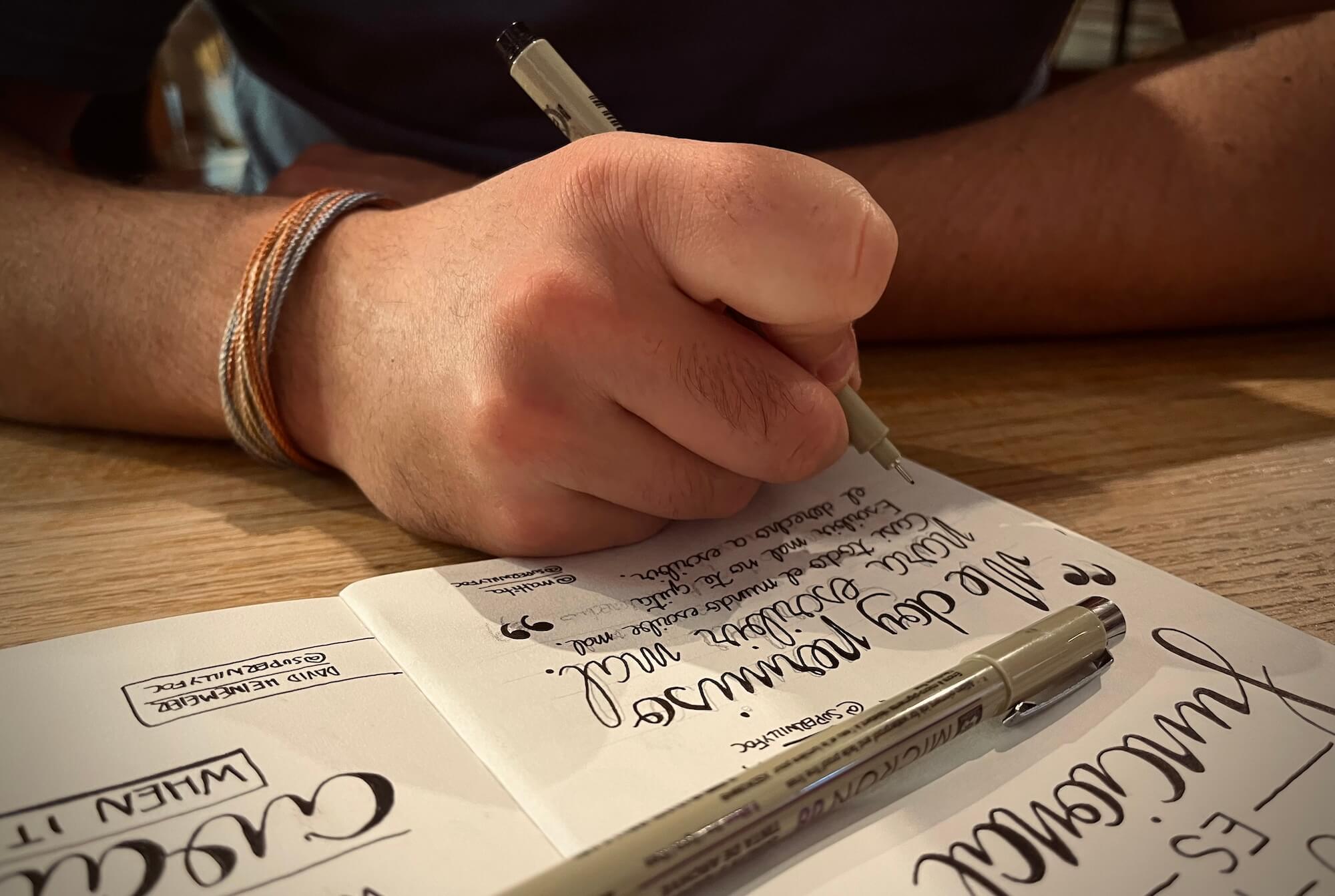 Escribiendo la cita en el cuaderno en una cafetería. Foto del cuaderno sobre la mesa, abierto con la página en la que está manuscrita la cita de la semana