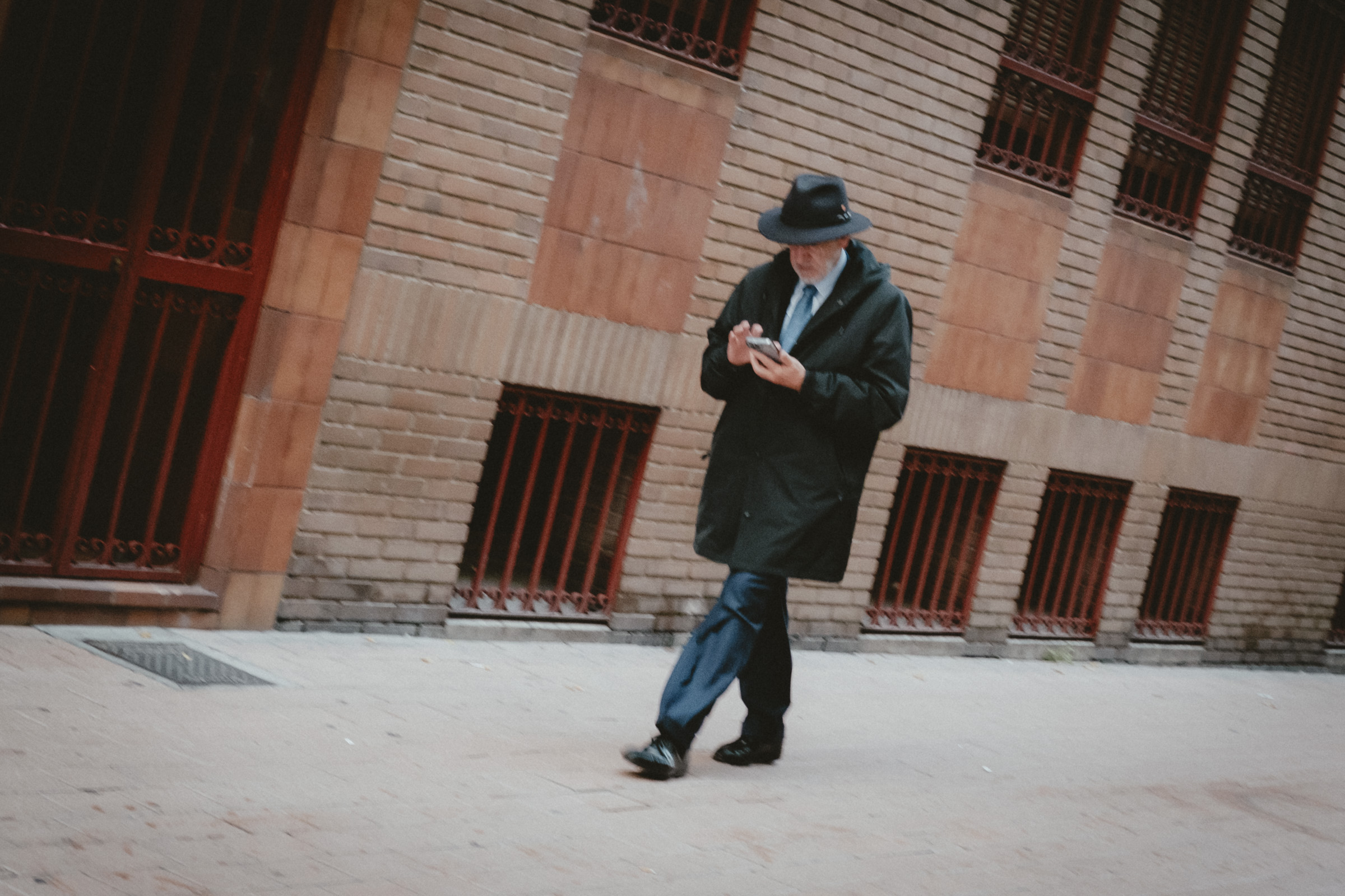 De camino al trabajo. Señor paseando mirando el móvil y vestido muy elegante, con sombrero y corbata