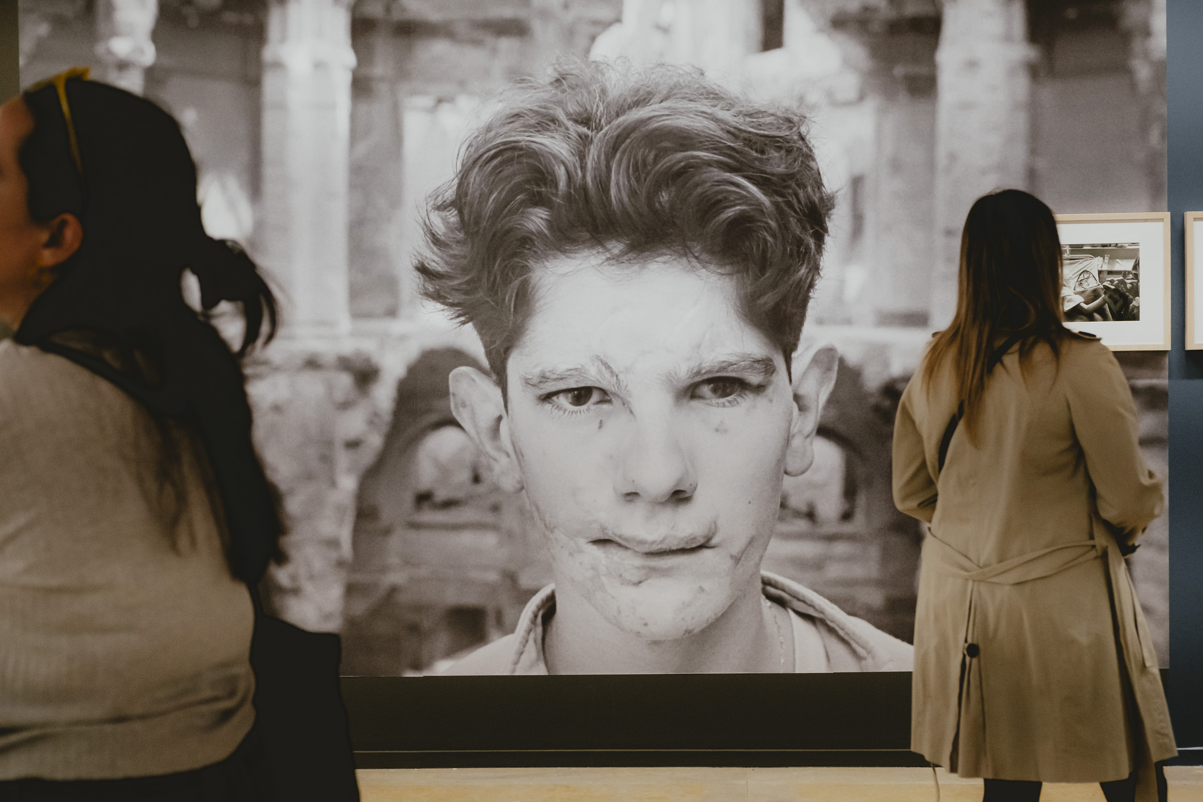 En la exposición "Vidas minadas" de Gervasio Sánchez, expuesta en La Lonja de Zaragoza. El protagonista de su fotografía es Adis Smajic (Bosnia-Herzegovina). Foto de una fotografía impresa a gran tamaño y dos mujeres en la sala mirando en otras direcciones