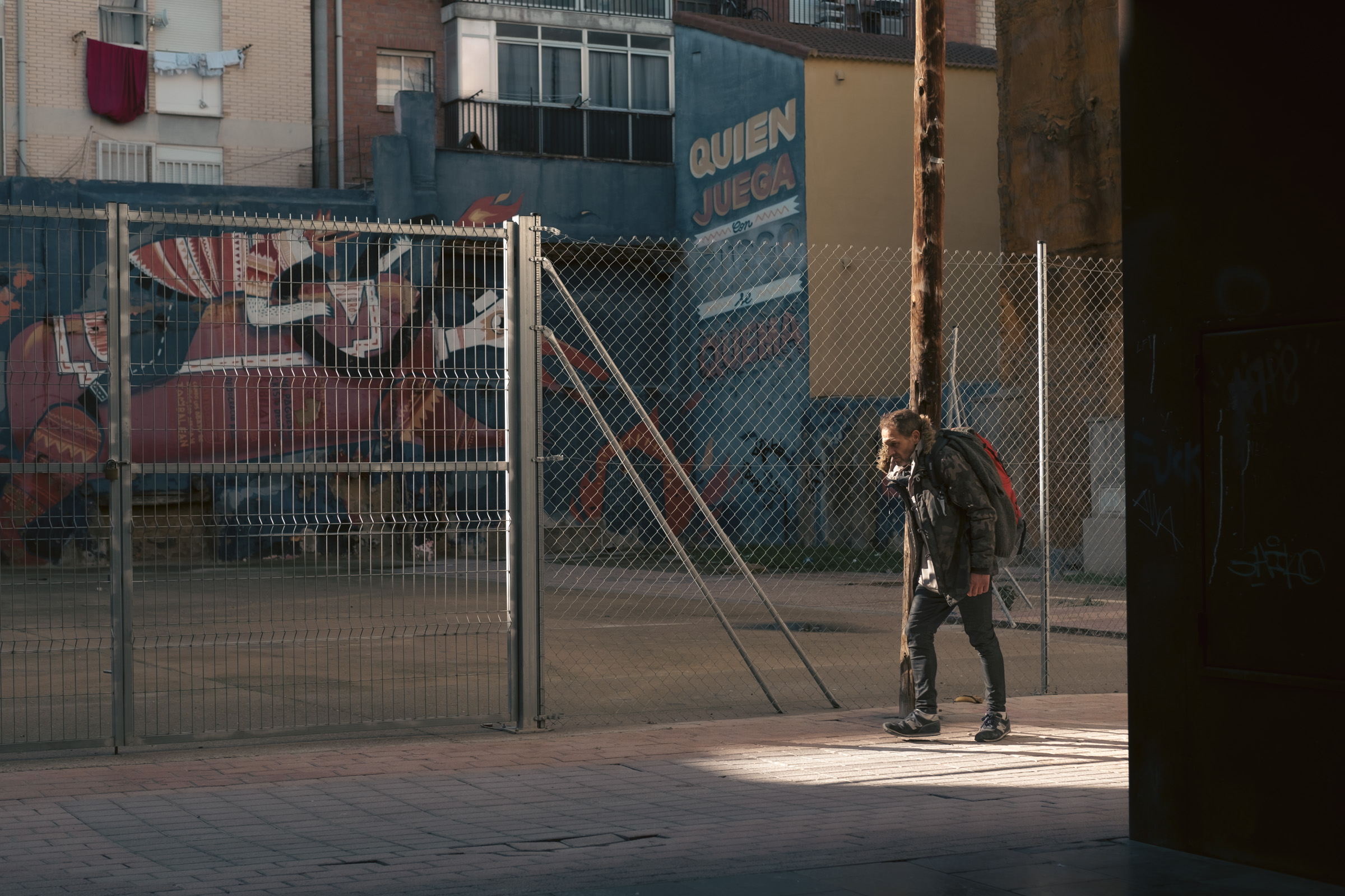 Señor paseando con una mochila y pasando justamente por el único punto de la calle que es iluminado por los rayos del sol