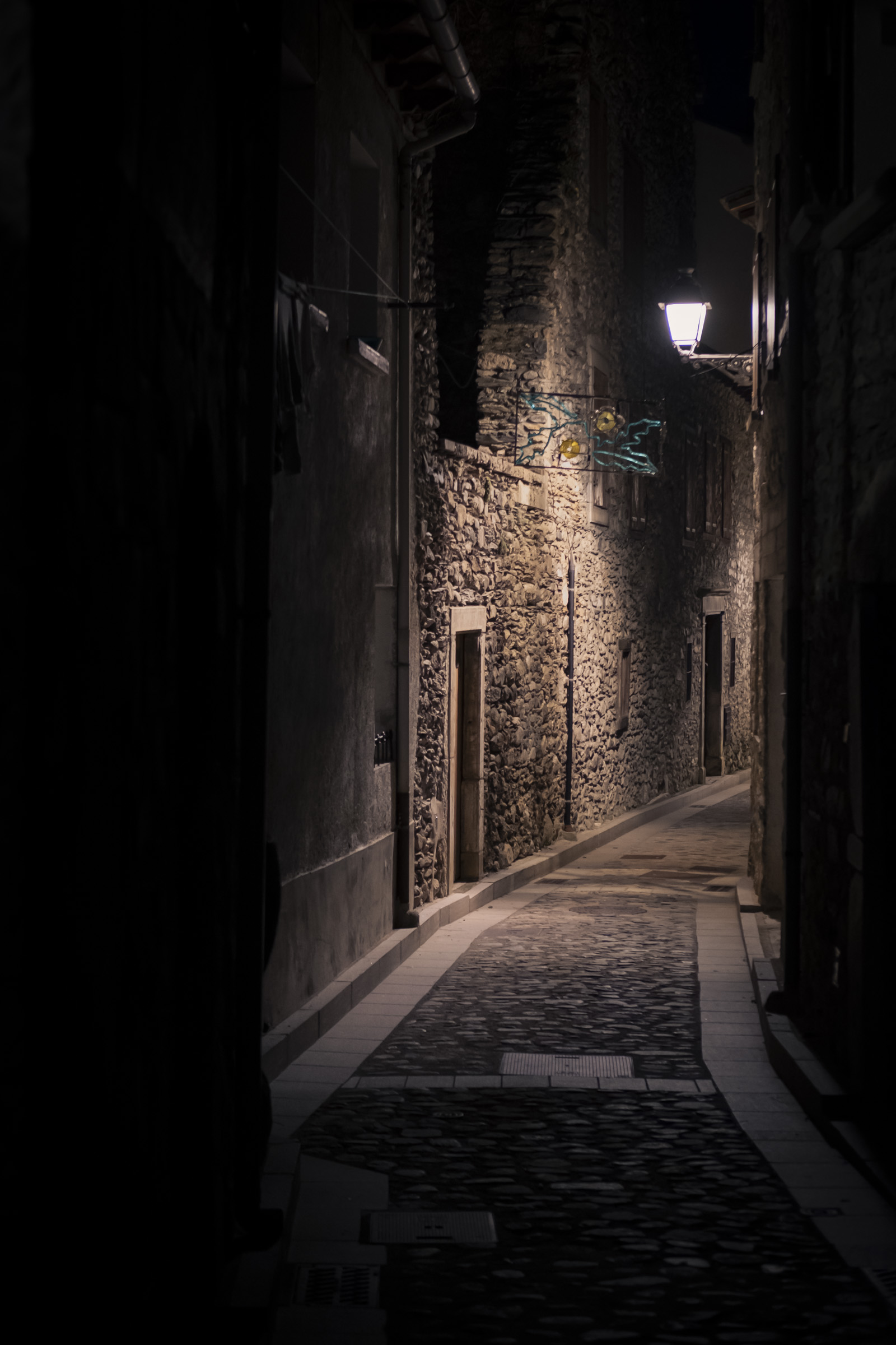 Las calles de Benasque a finales de noviembre. Una calle oscura de un pueblo pirenaico, con las paredes y el piso de piedra tradicional, iluminada parcialmente por una farola