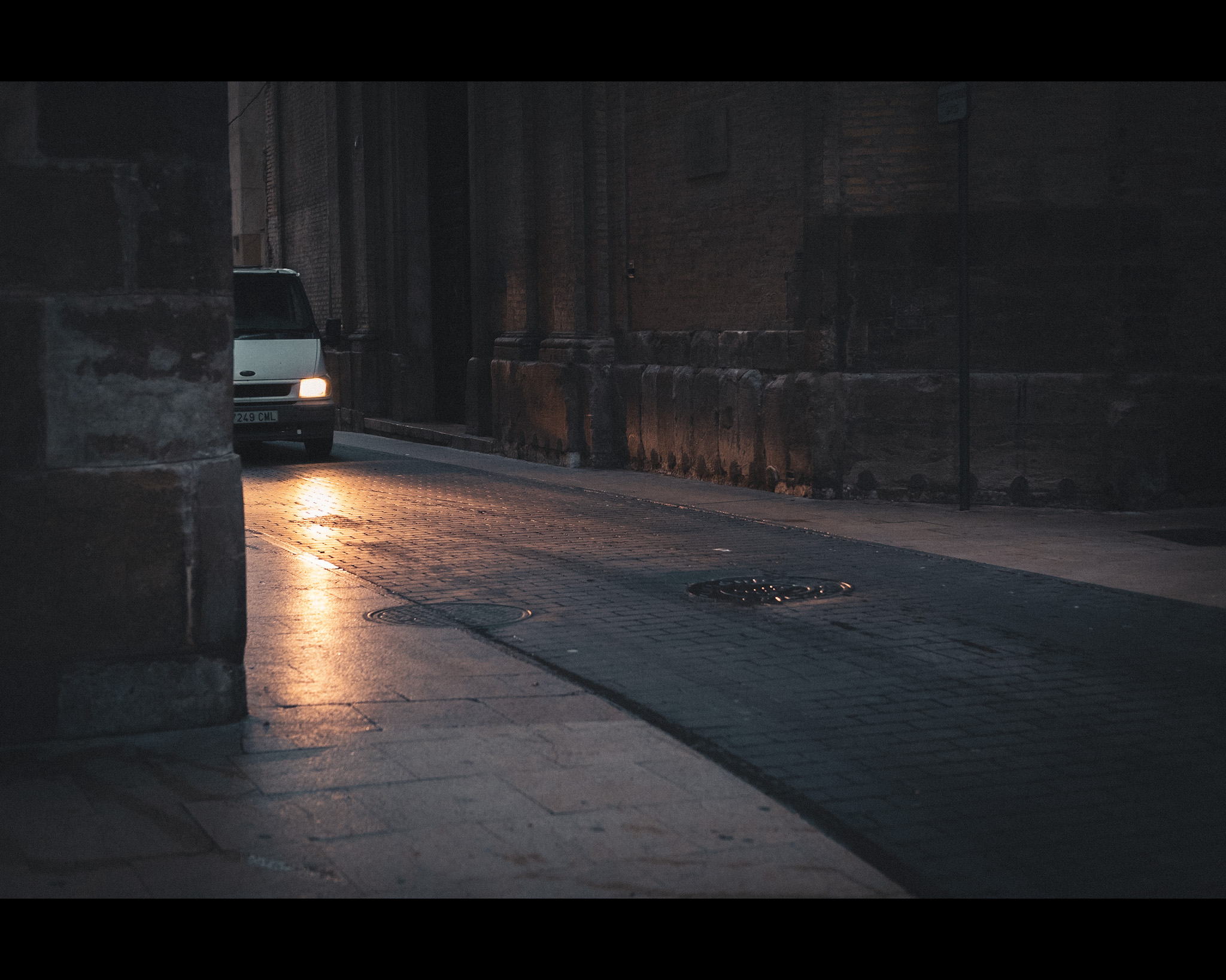 Furgoneta apareciendo e iluminando la calle por la mañana. Una furgoneta aparece por la calle detrás de una esquina, con un ambiente frío del amanecer y el contraste con los faros cálidos del vehículo