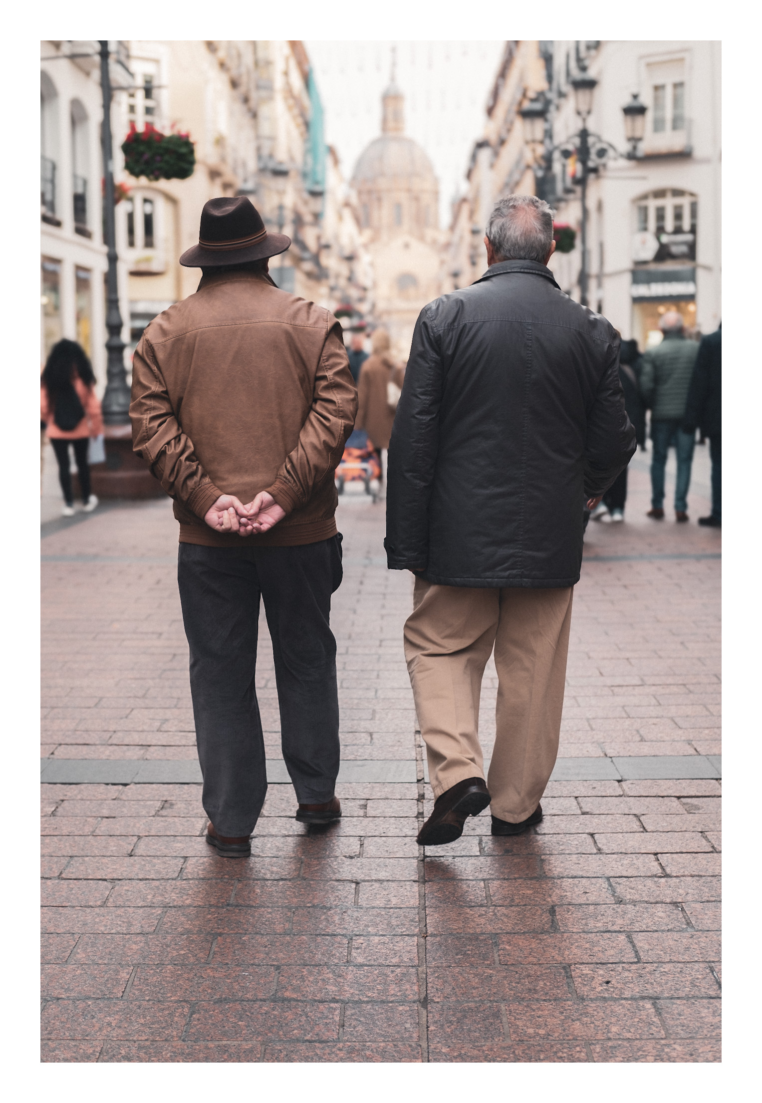 De paseo por la calle Alfonso en Zaragoza. Con el Pilar de frente. Dos señores de espaldas, caminando por la calle Alfonso con El Pilar delante y sus posturas parecen simétricas