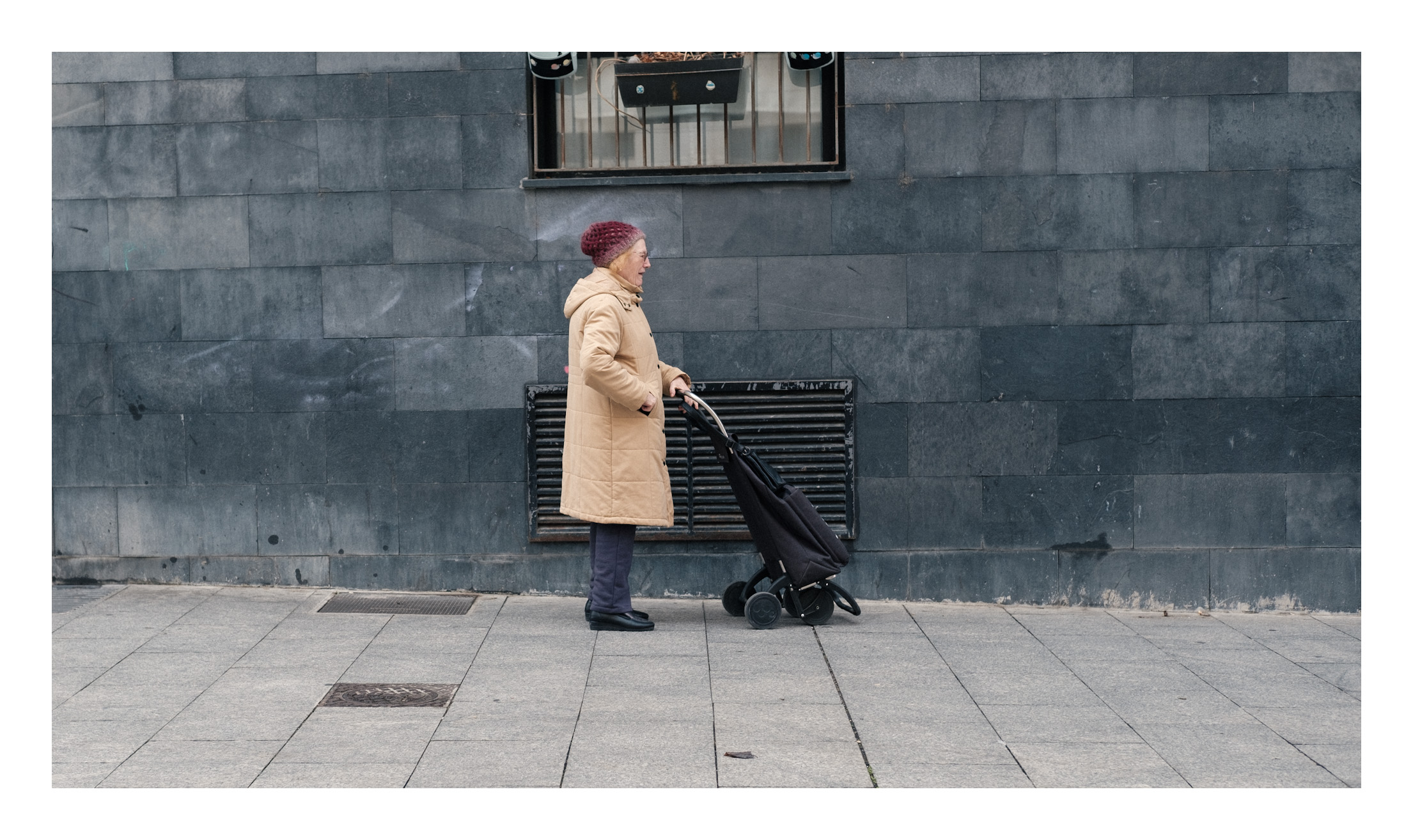 Momento de ir a comprar al mercado. Una señora se dirige al mercado con su carro de la compra y se detiene para coger un poquito de aire