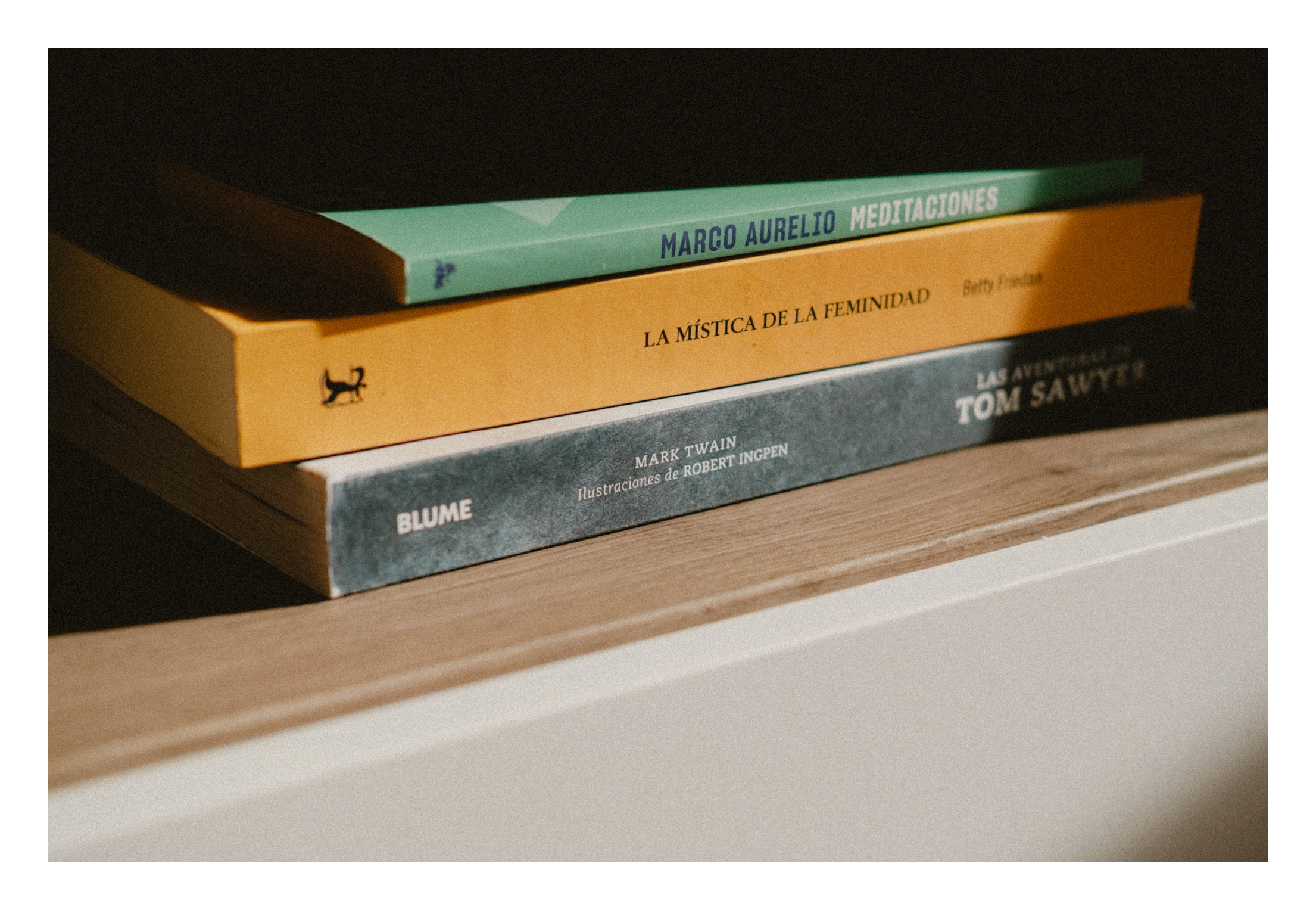 Libros con la luz del atardecer. Primer plano de unos libros de varios colores en una estantería con la luz del sol incidiendo de lado y creando zonas de sombras