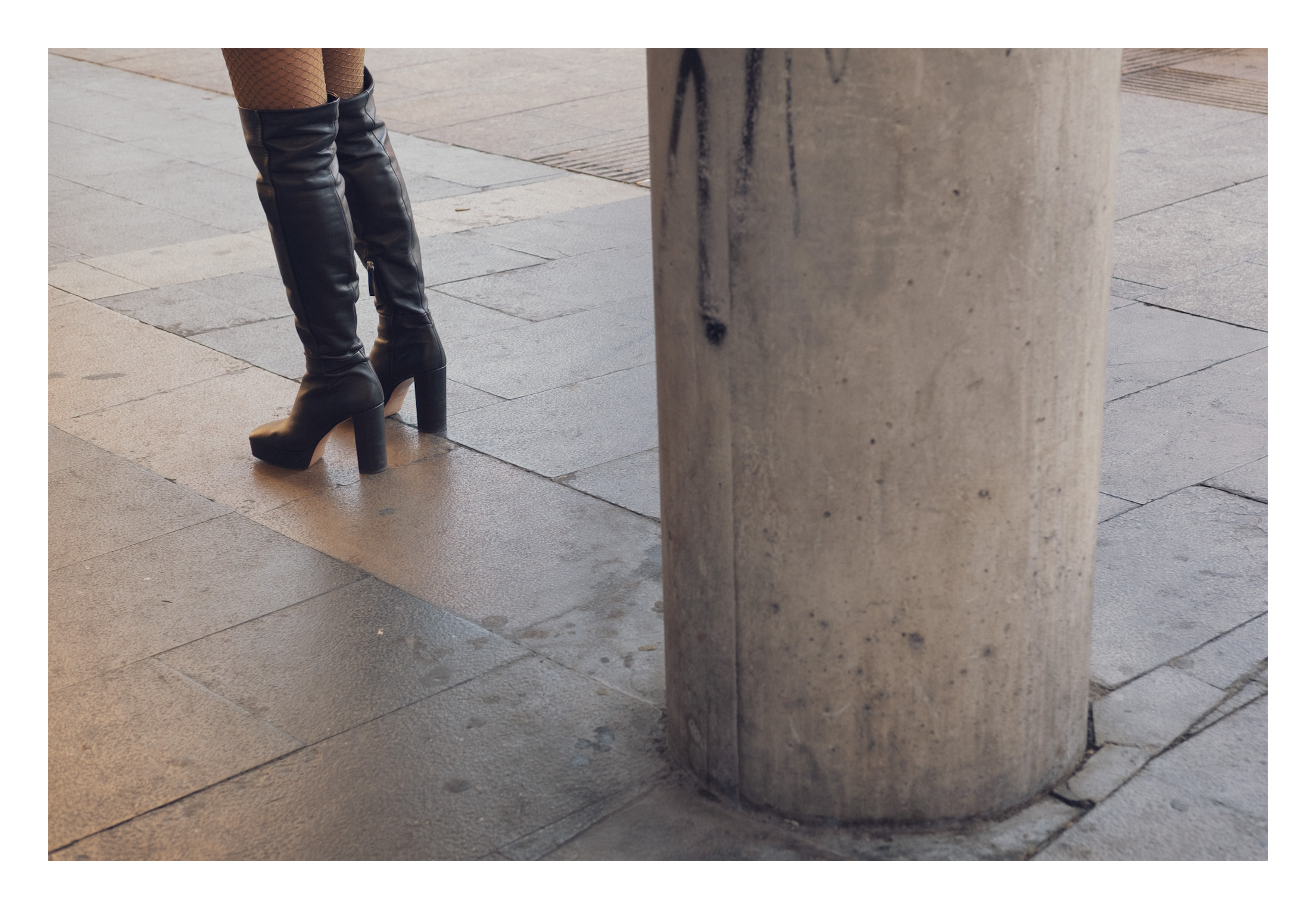 Columna, botas y medias de rejilla. Se ve una columna de cemento y una chica con botas de piel y medias de rejilla cortada por el encuadre por encima de las rodillas