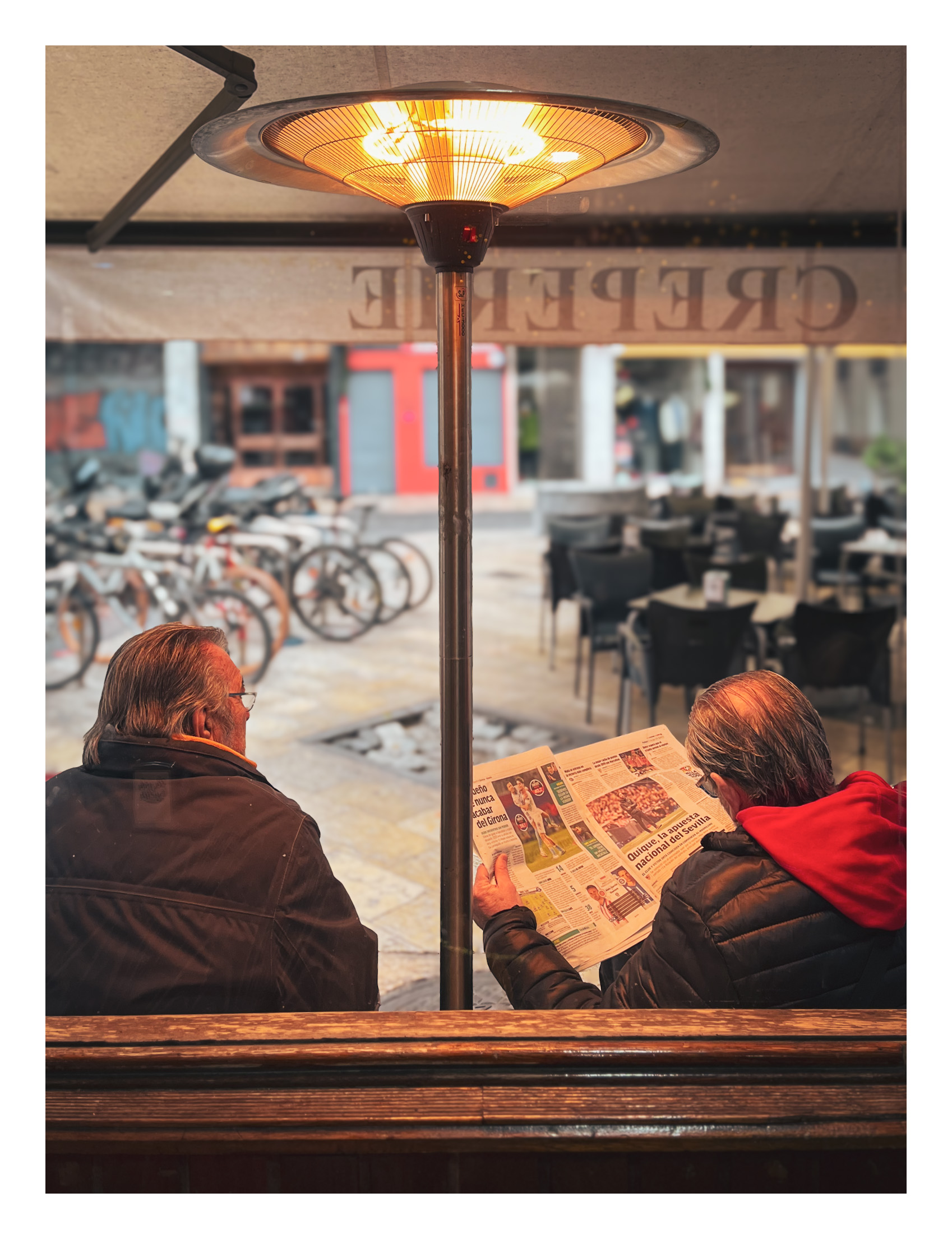 Café y periódico mañanero en invierno. Dos señores, al punto de la mañana, tomando café en una terraza y leyendo el periódico en papel bajo una estufa de gas
