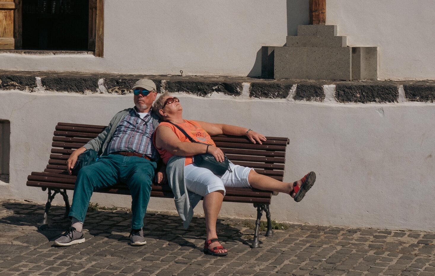 Una pareja descansa en un banco tomando el sol con ímpetu y con una cruz y una paloma detrás de ellos