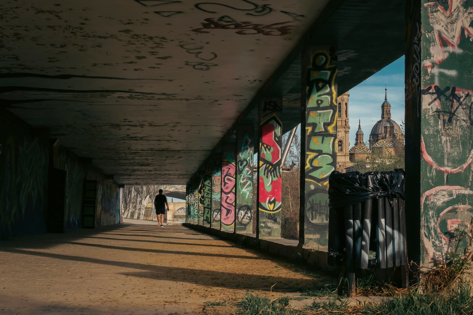 Pasaje con grafitis en la ribera con El Pilar de fondo y gente paseando