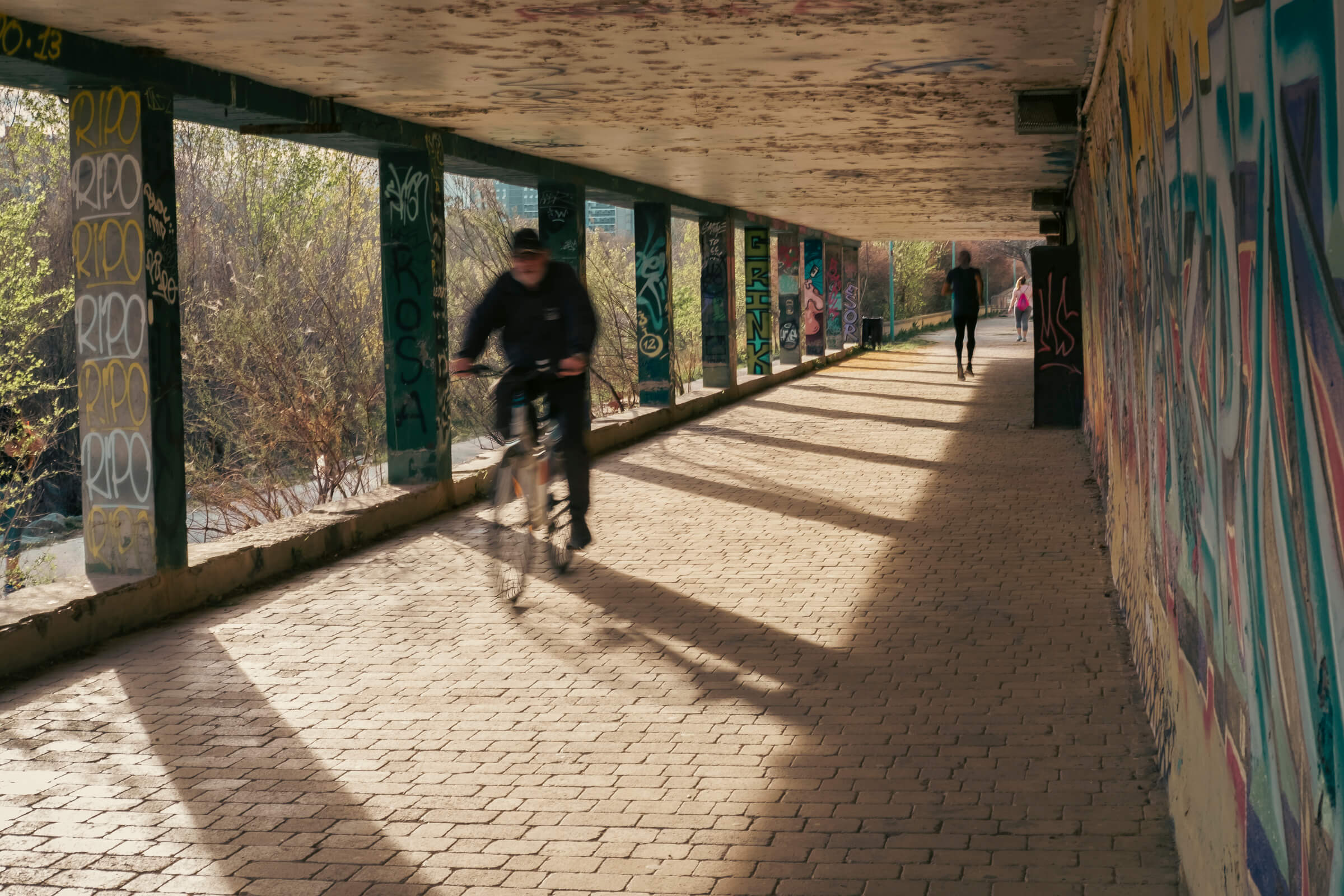 Pasaje con grafitis en la ribera y gente haciendo deporte