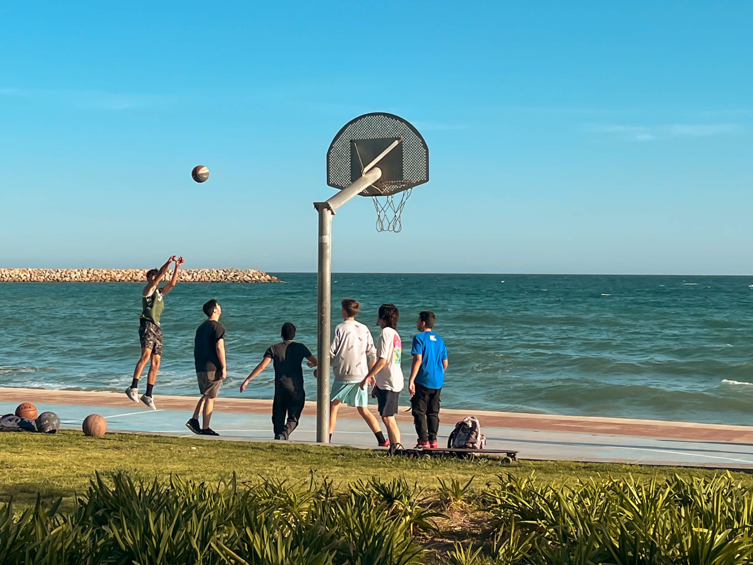 Intento de triple en la playa de Cambrils (Tarragona). Grupo jugando al baloncesto en el paseo marítimo al lado de la playa