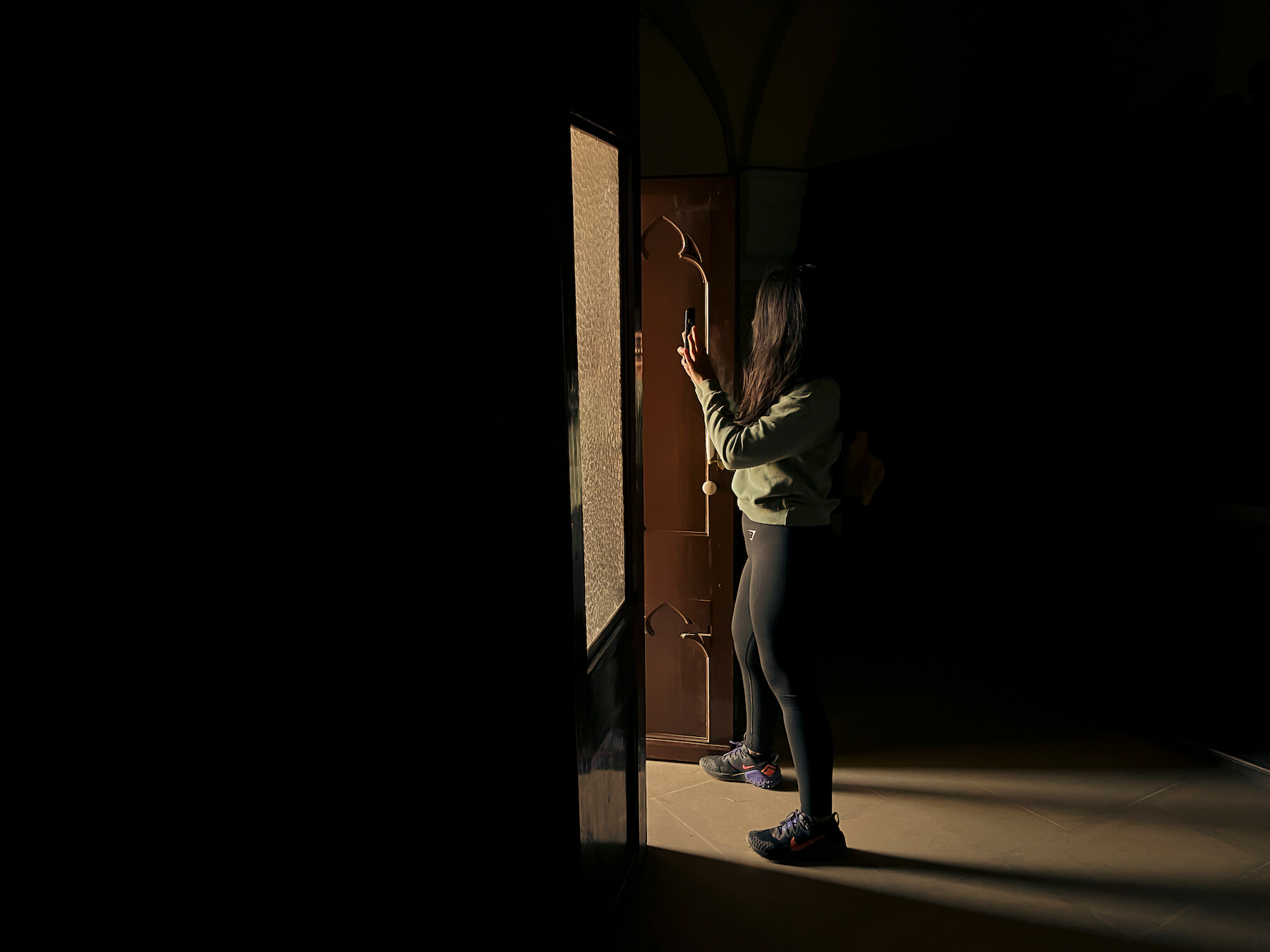 Laura haciendo una foto con el móvil, desde dentro de la ermita y enfocando al exterior, con la luz iluminándola.