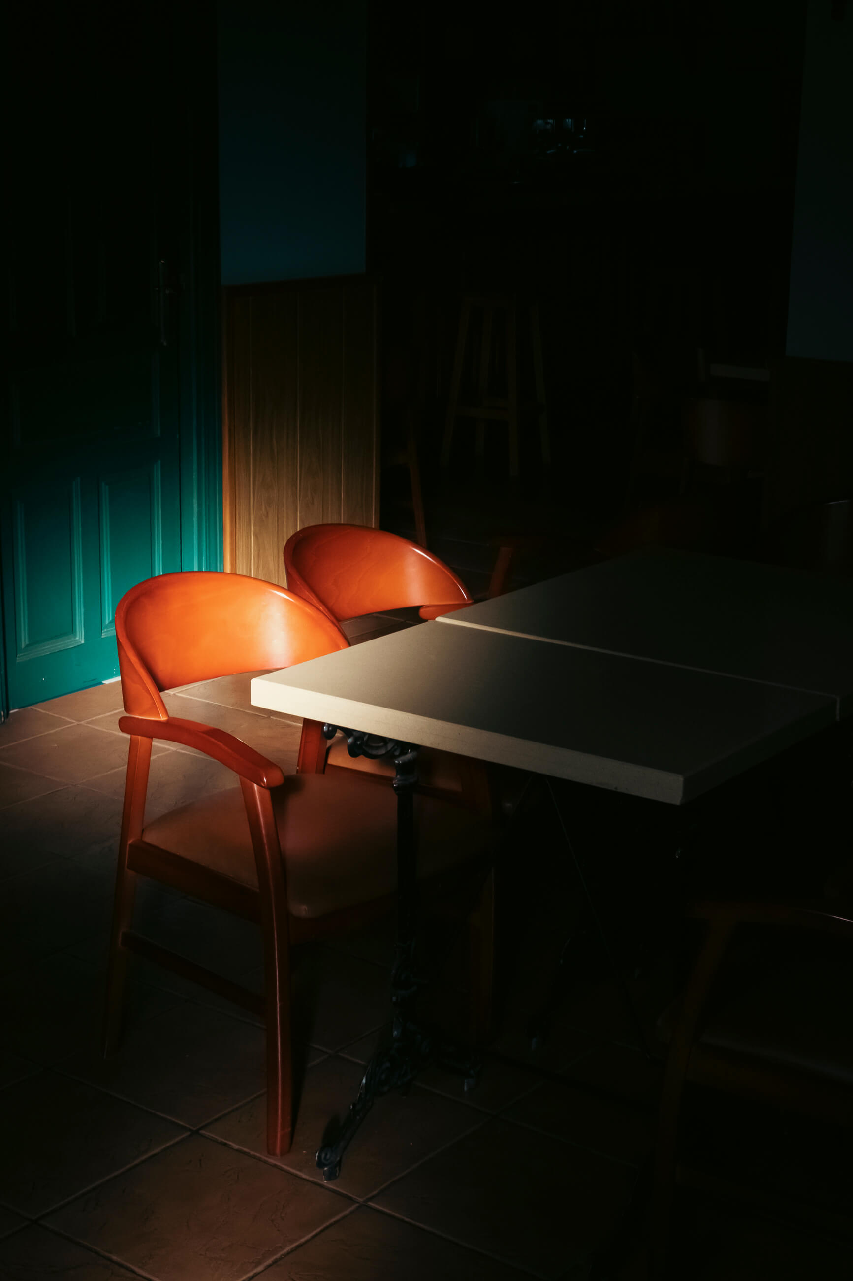 En un bar de hotel está muy oscuro salvo la zona que ilumina la luz del amanecer que empieza a entrar por una ventana y que ilumuna una silla y una mesa muy antiguas