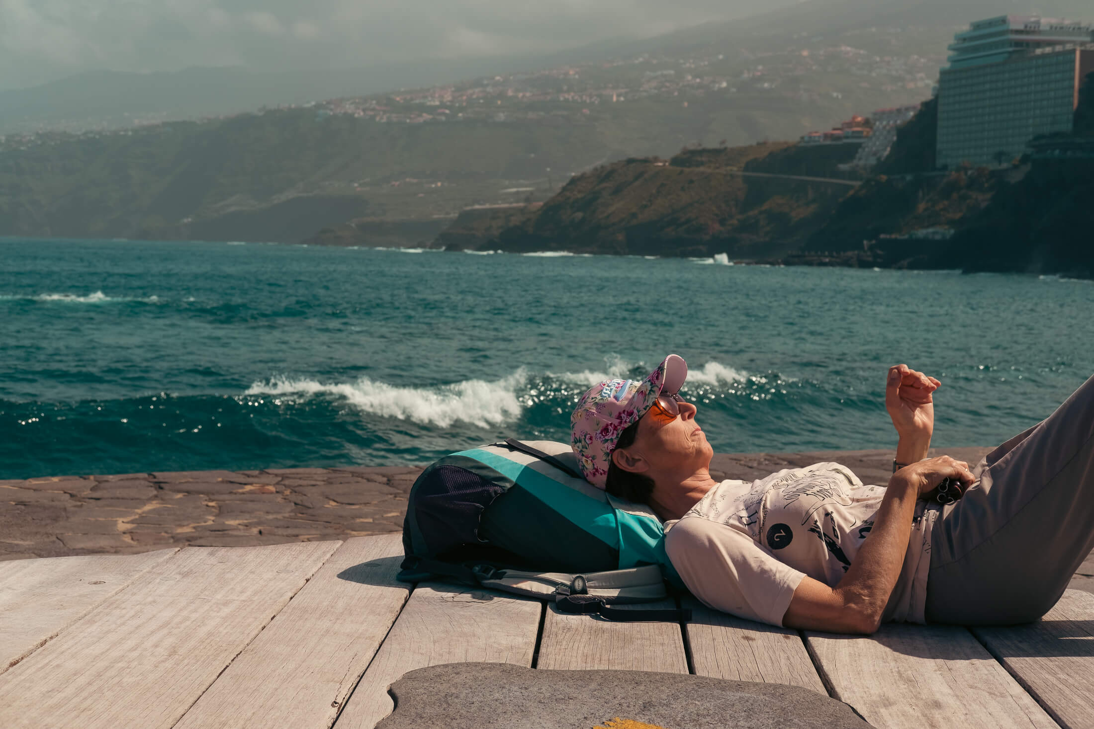 Mujer tumbada en un banco del paseo tomando el sol mientras escucha las olas del mar y la música en directo